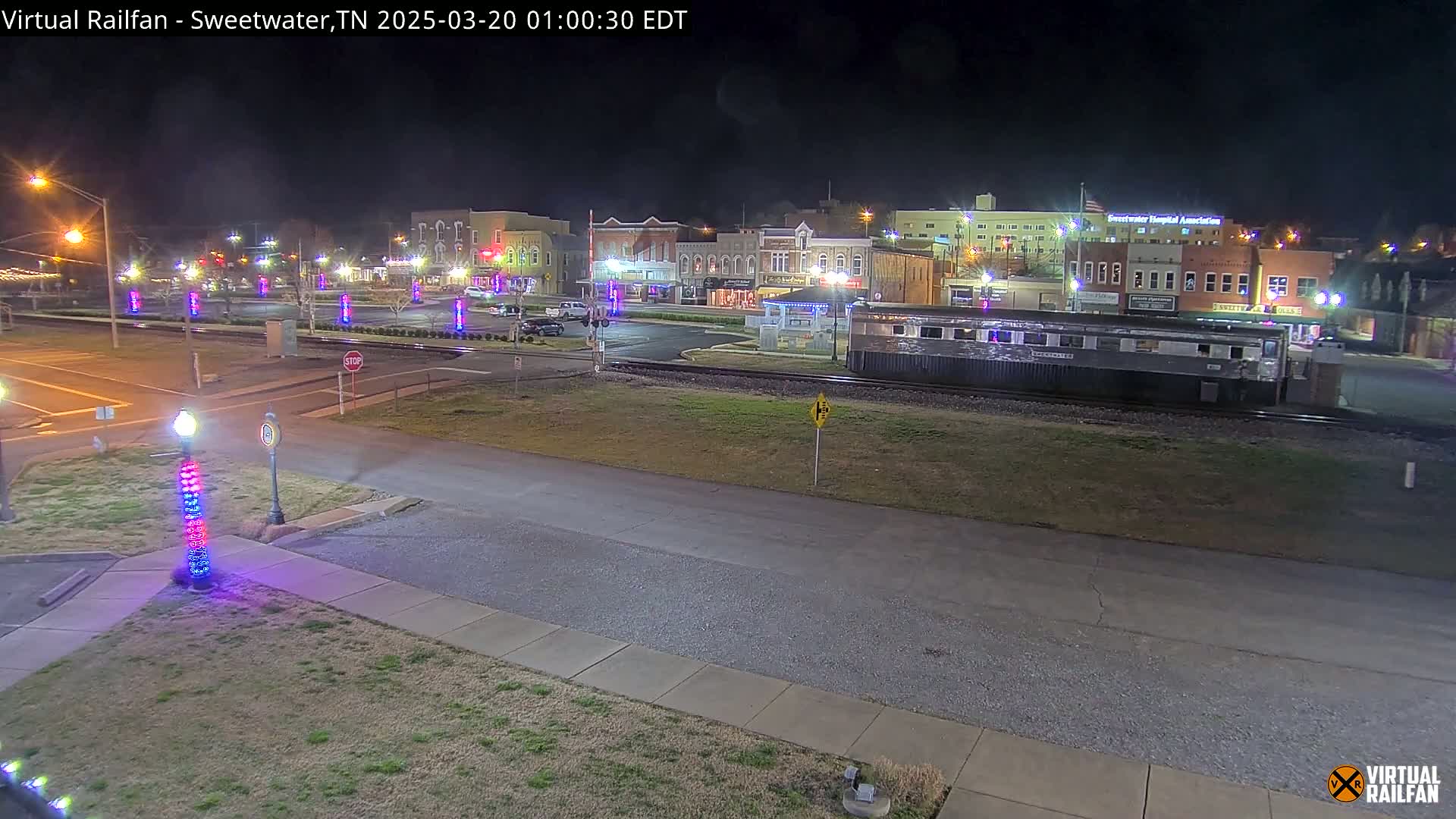 A nighttime view of a town square with several buildings, a railway car, and decorative lights illuminating the area.