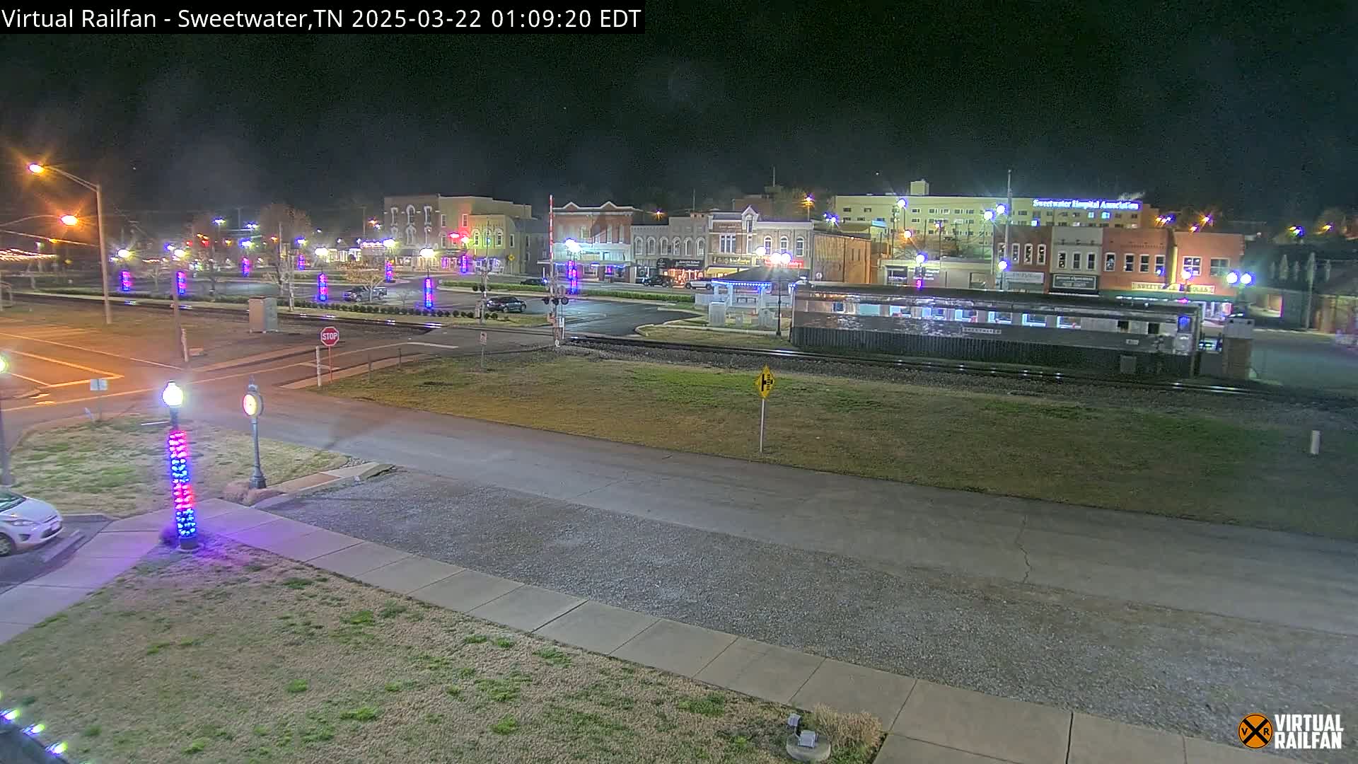 A nighttime view of a town square with a train car parked nearby, under clear skies.