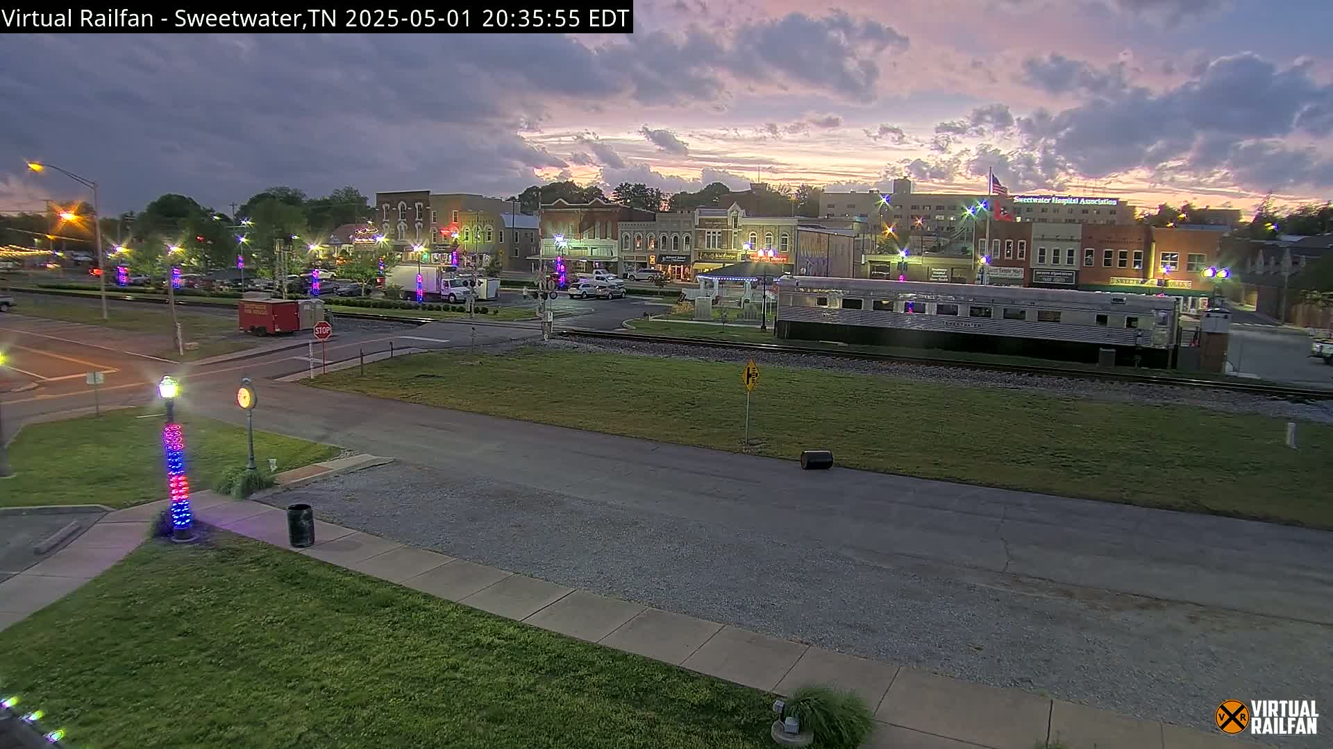 A twilight view of a small town's downtown area, featuring a railway car and buildings, under a partly cloudy sky.