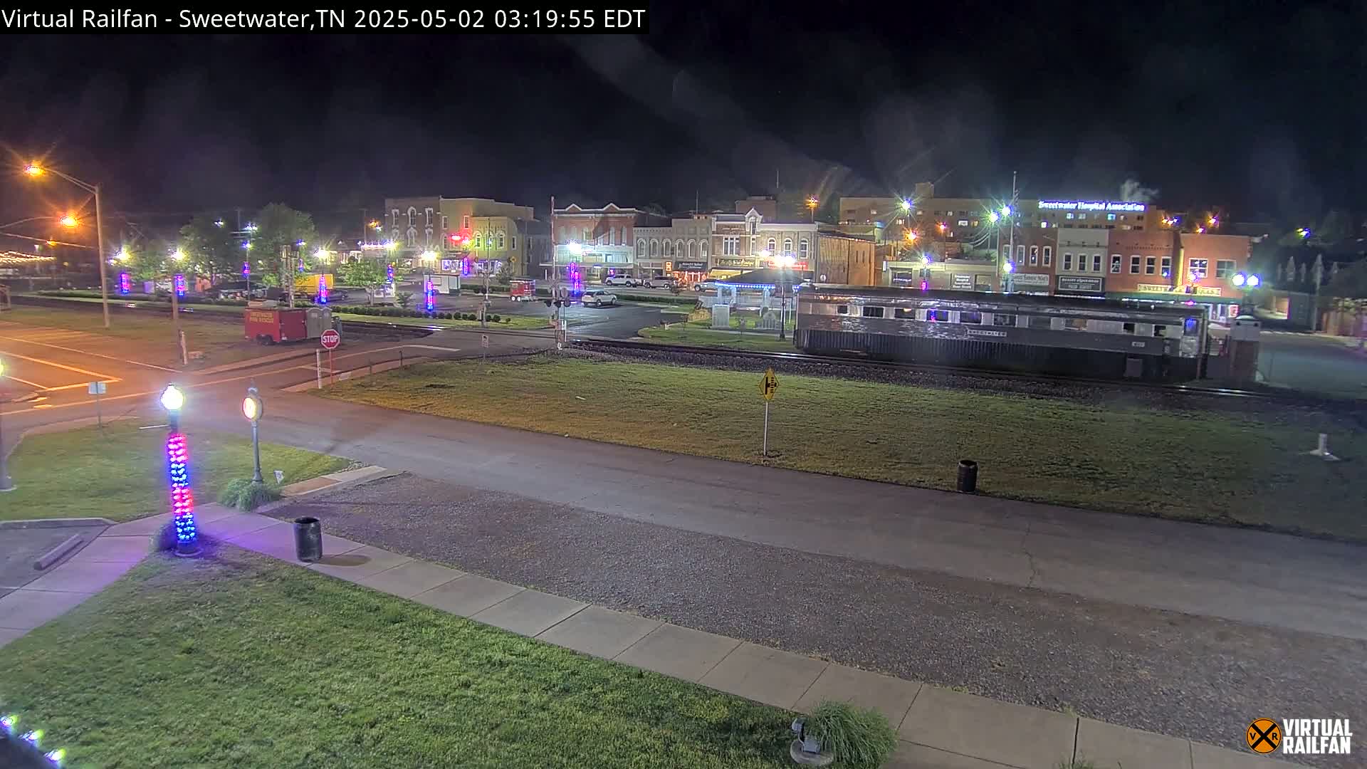 A nighttime view of a town square with a train car parked nearby, under a clear sky.