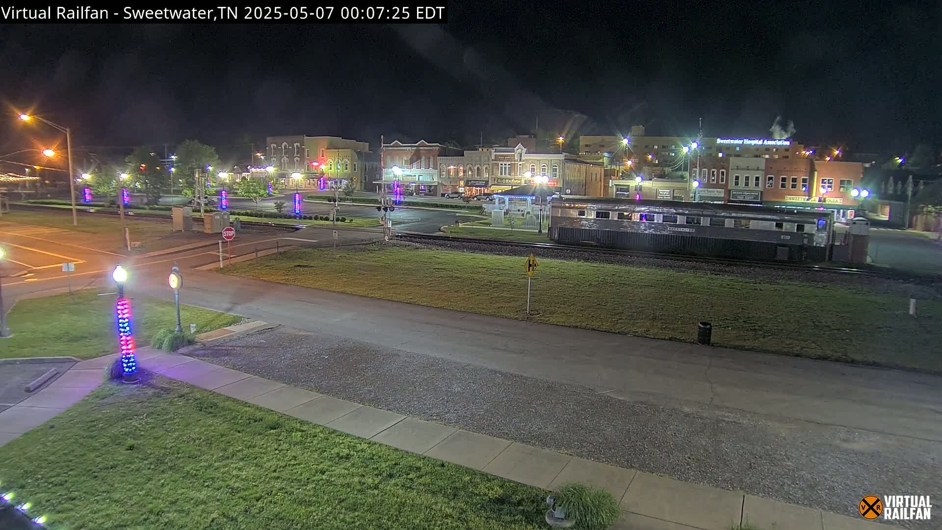 A nighttime view of a small town square with a train car parked nearby, illuminated by streetlights.