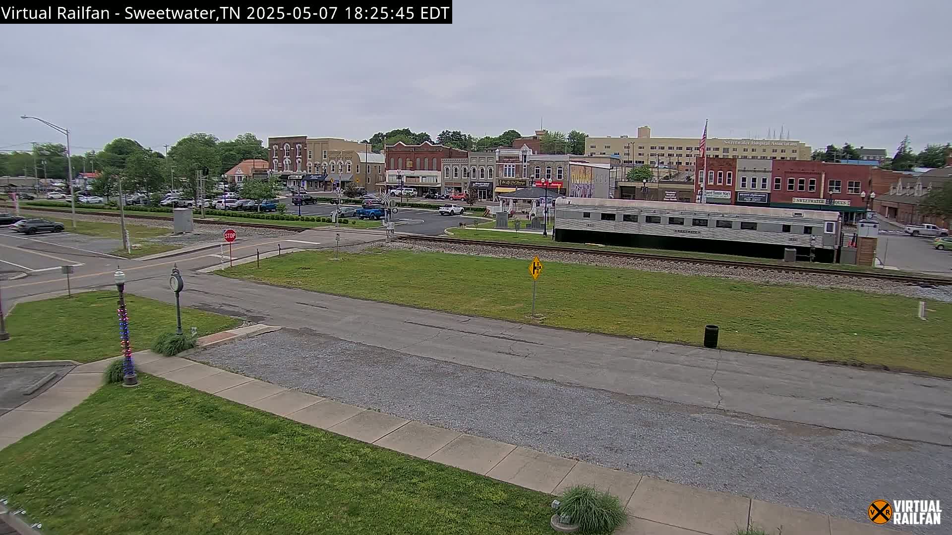 A mostly sunny view of a small town's downtown area, including a train car parked on railroad tracks, under an overcast sky.