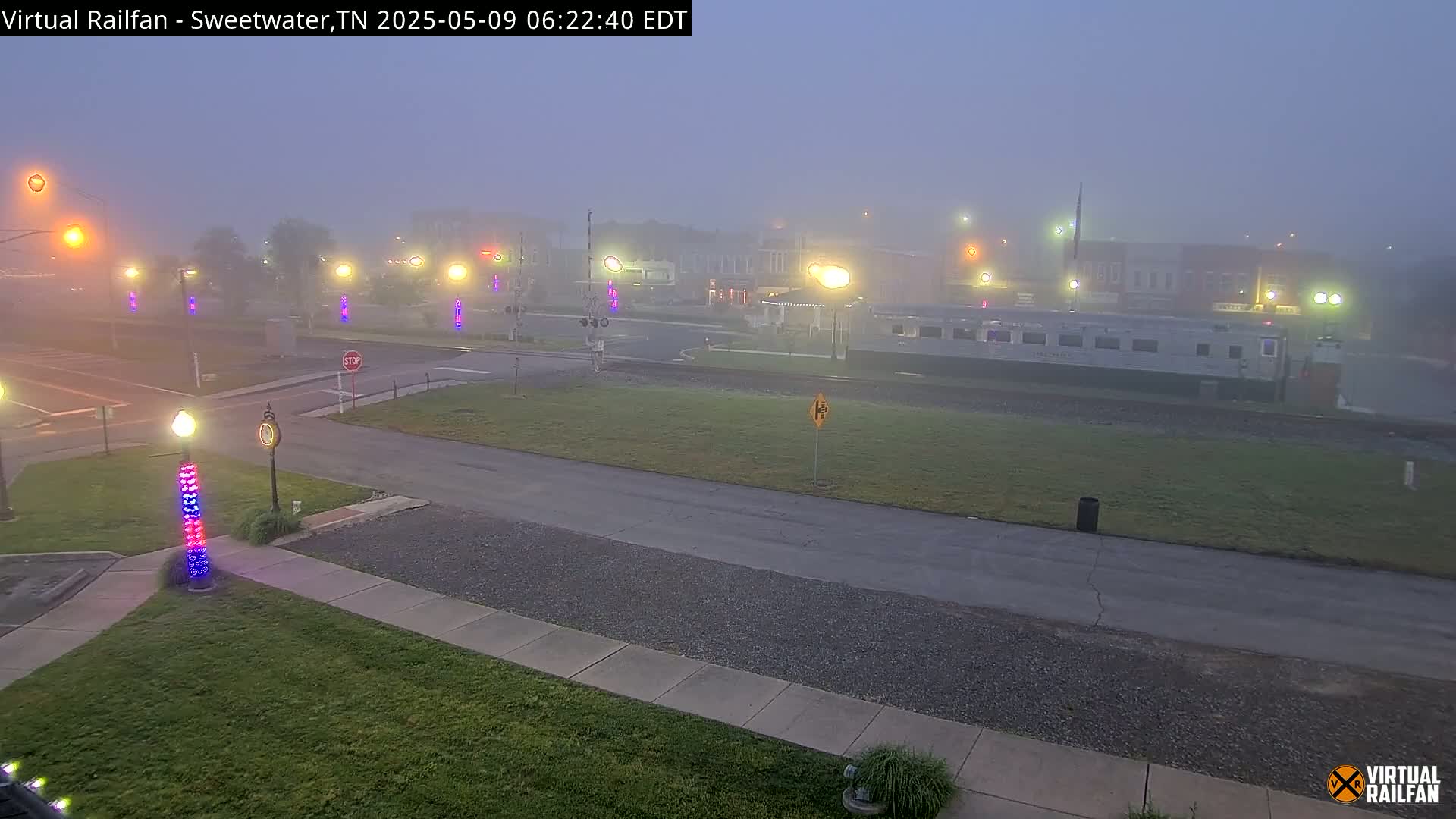A foggy town square with a train car visible in the distance, streetlights illuminating the scene.