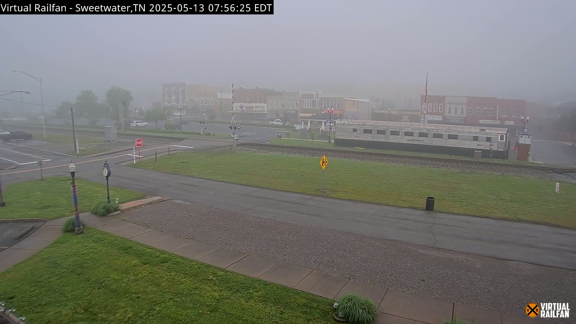 A foggy view of a town square shows a train car parked on a track next to a street and several buildings.