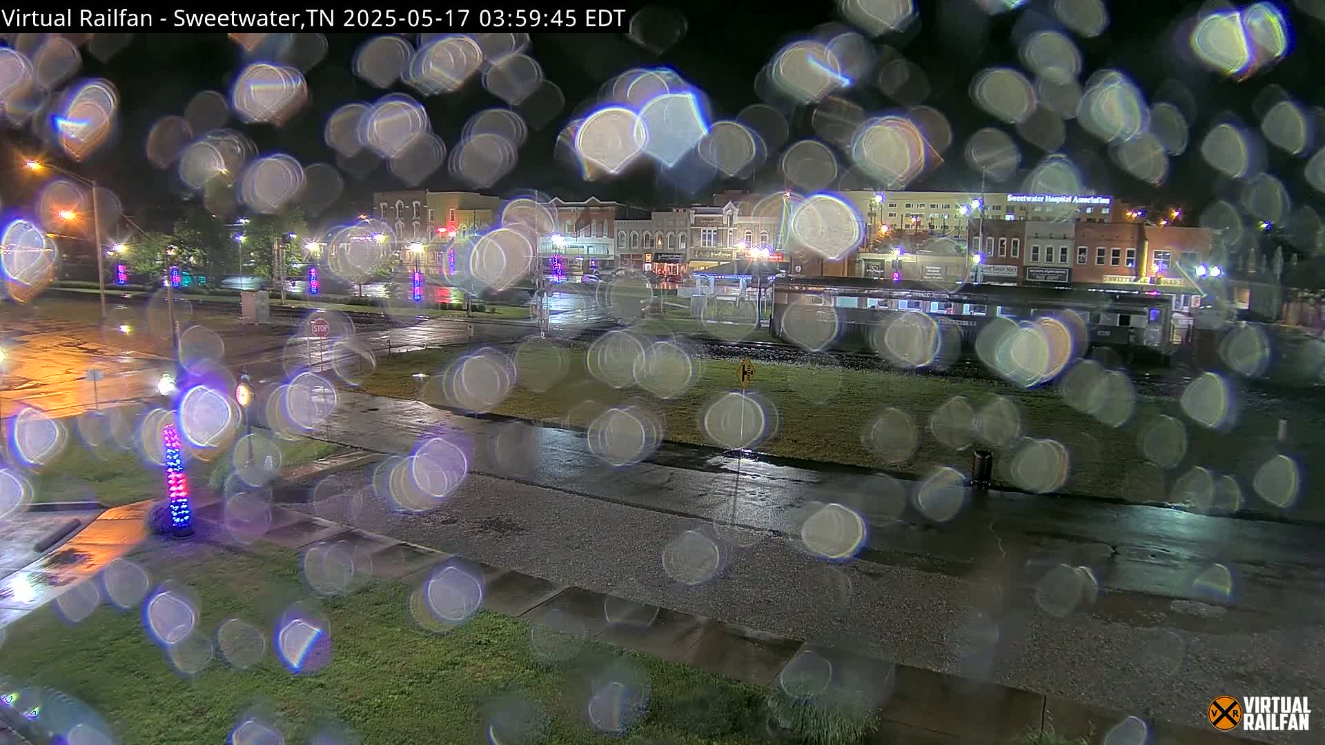 A nighttime view of a rain-slicked town square with buildings and streetlights visible through rain-covered glass.