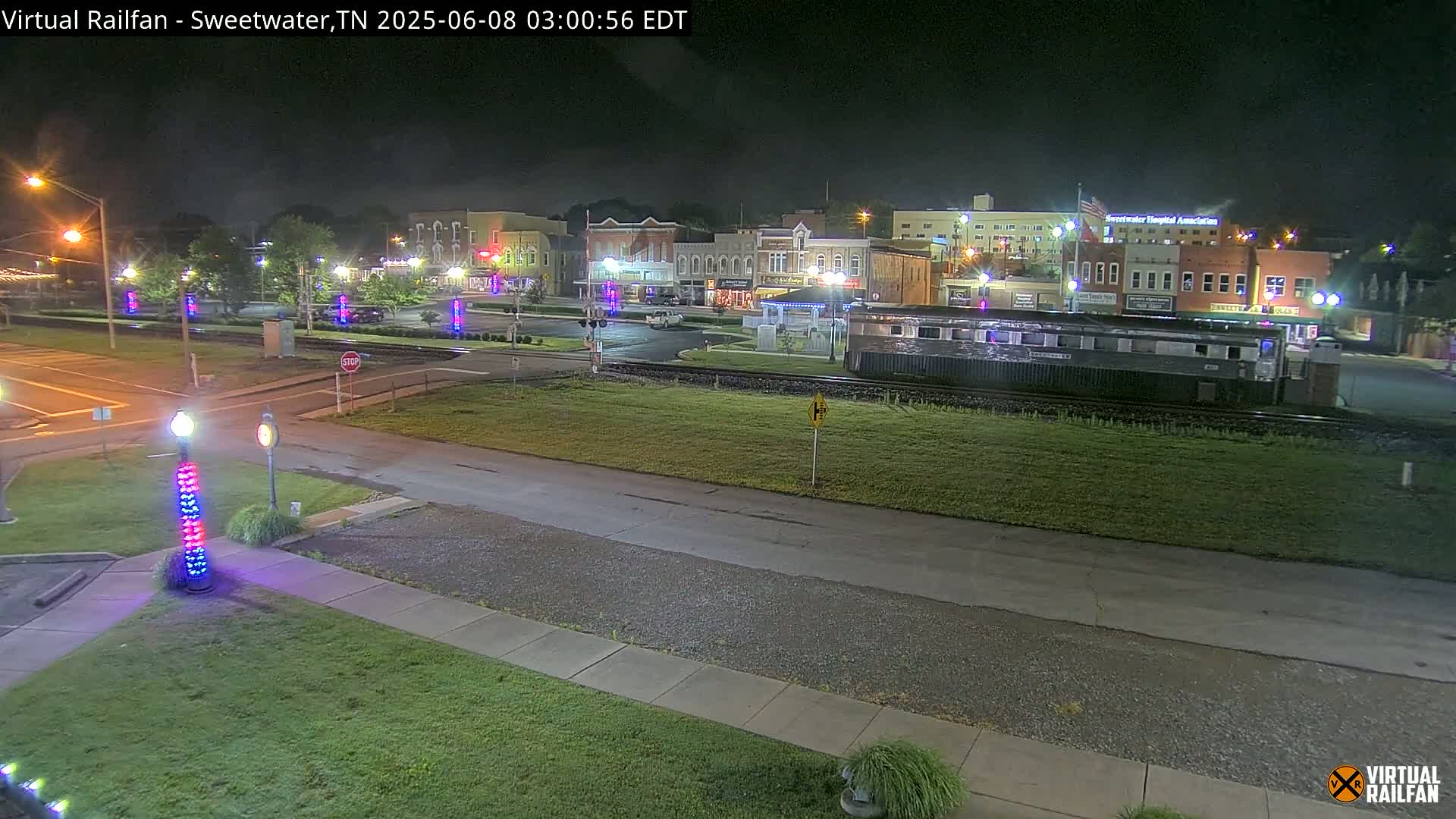 A nighttime view of a town square with several buildings, a train car, and decorative lights on lampposts.