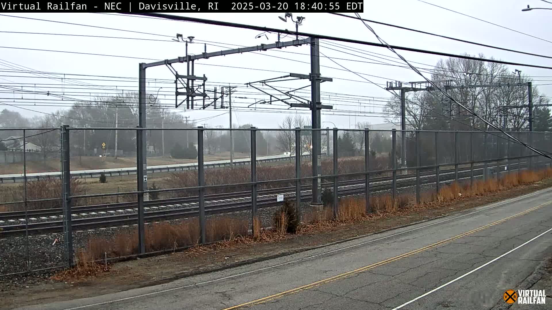 A view of train tracks behind a chain-link fence on an overcast day.