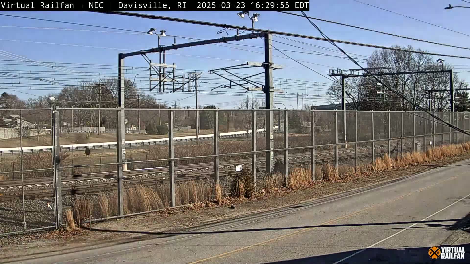 A view of train tracks behind a chain-link fence on a sunny day.