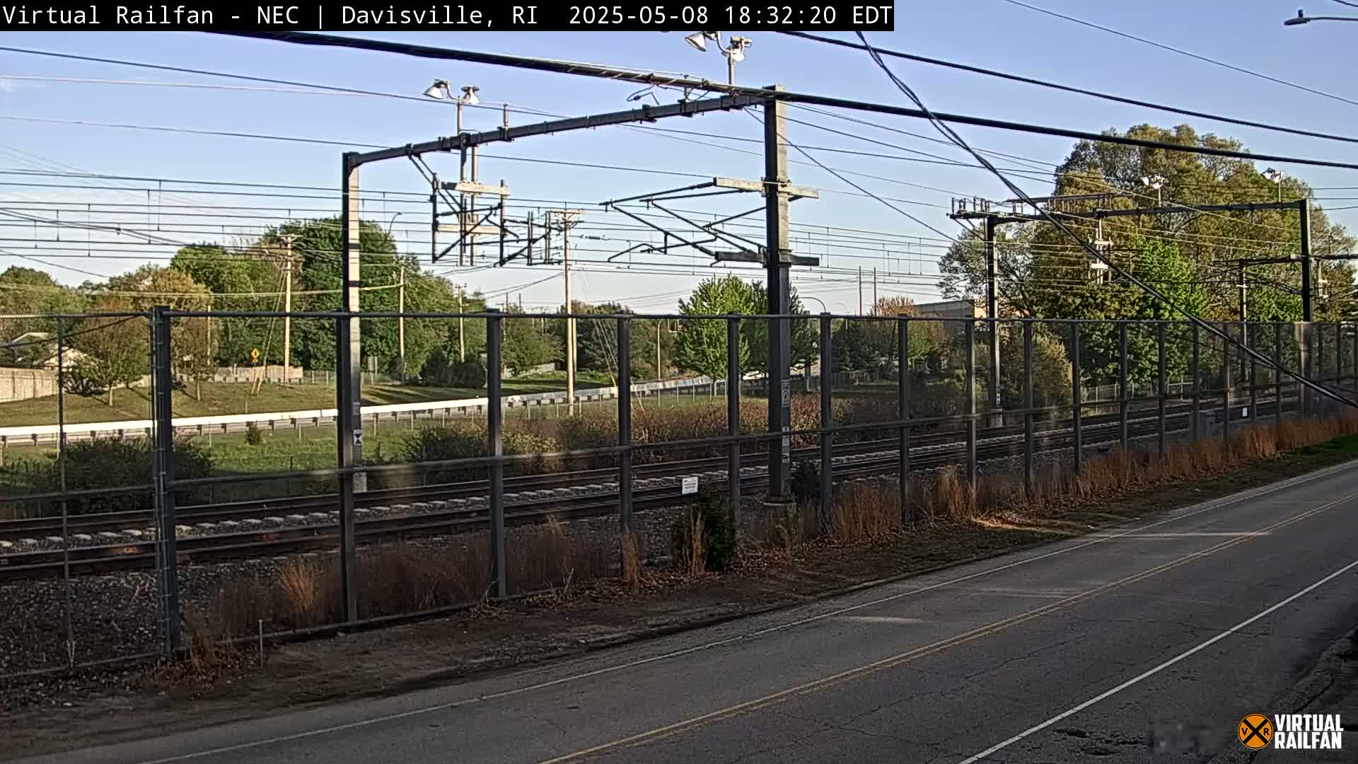 A view of railroad tracks behind a chain-link fence on a sunny day.