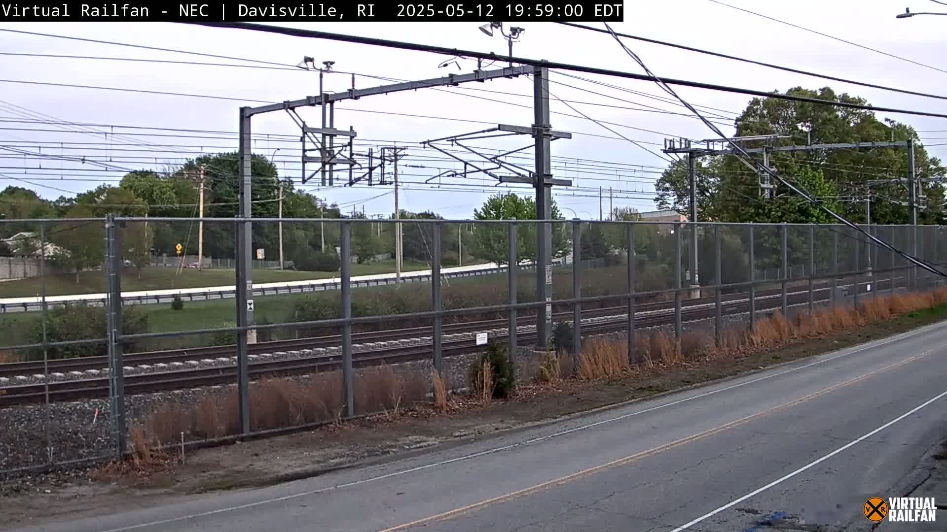 A view of railroad tracks behind a chain-link fence on an overcast day.