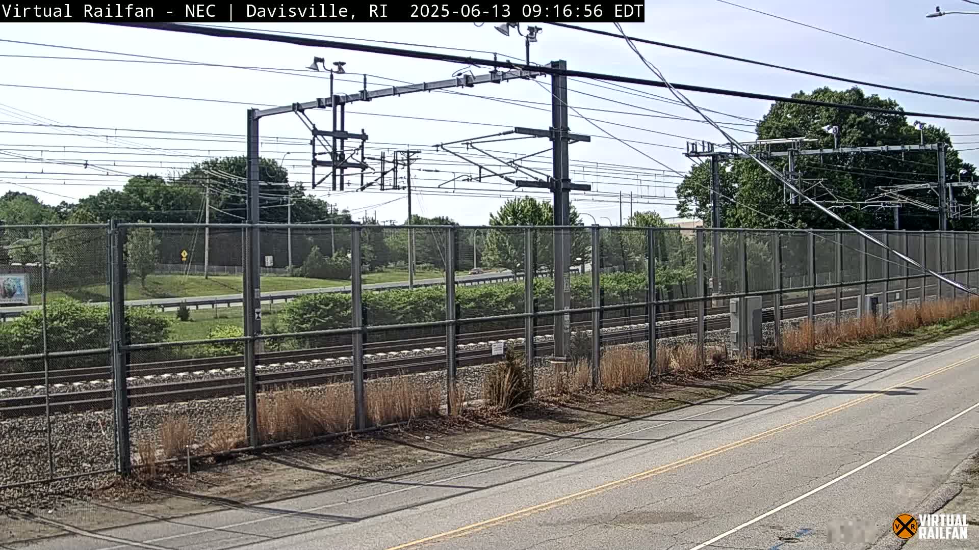 A view of railroad tracks behind a chain-link fence on a partly sunny day.