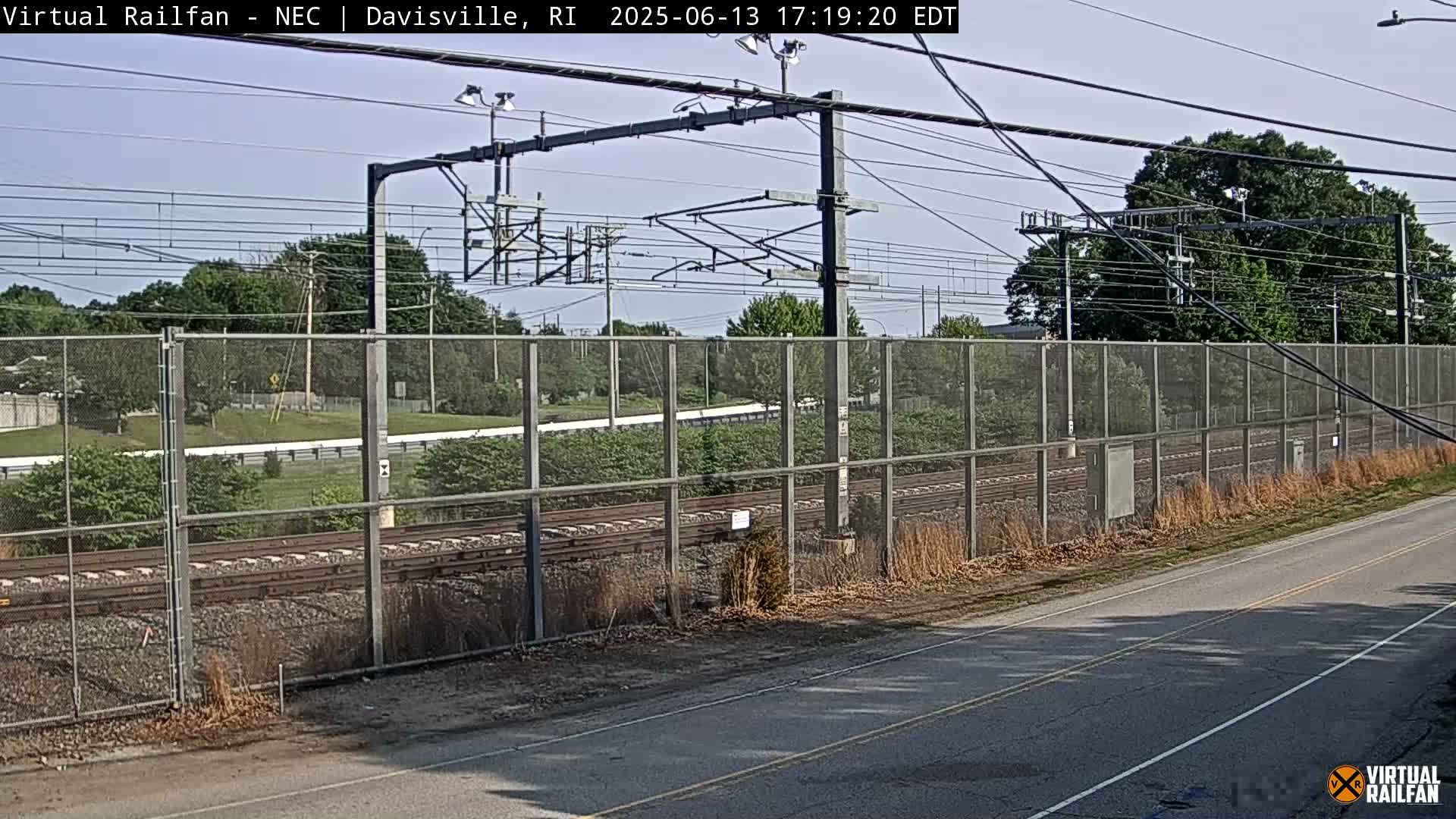 A view of railroad tracks behind a chain-link fence on a sunny day.