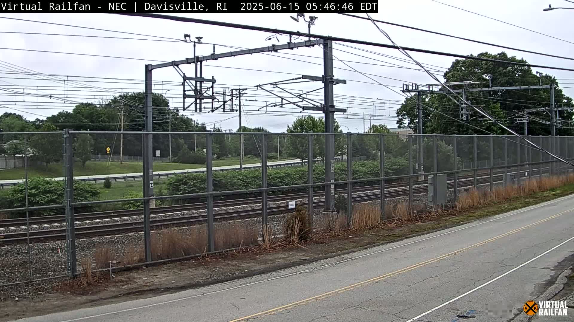 A view of railroad tracks behind a chain-link fence on an overcast day.