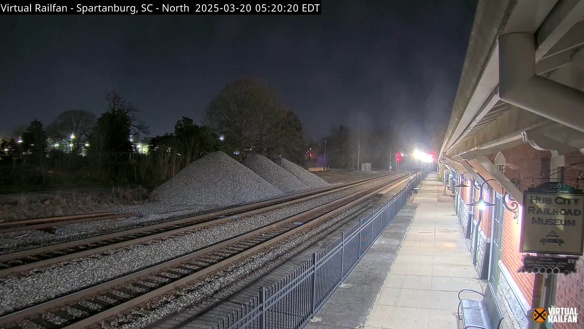 At night, railroad tracks extend from a train platform toward piles of gravel under a dark sky.