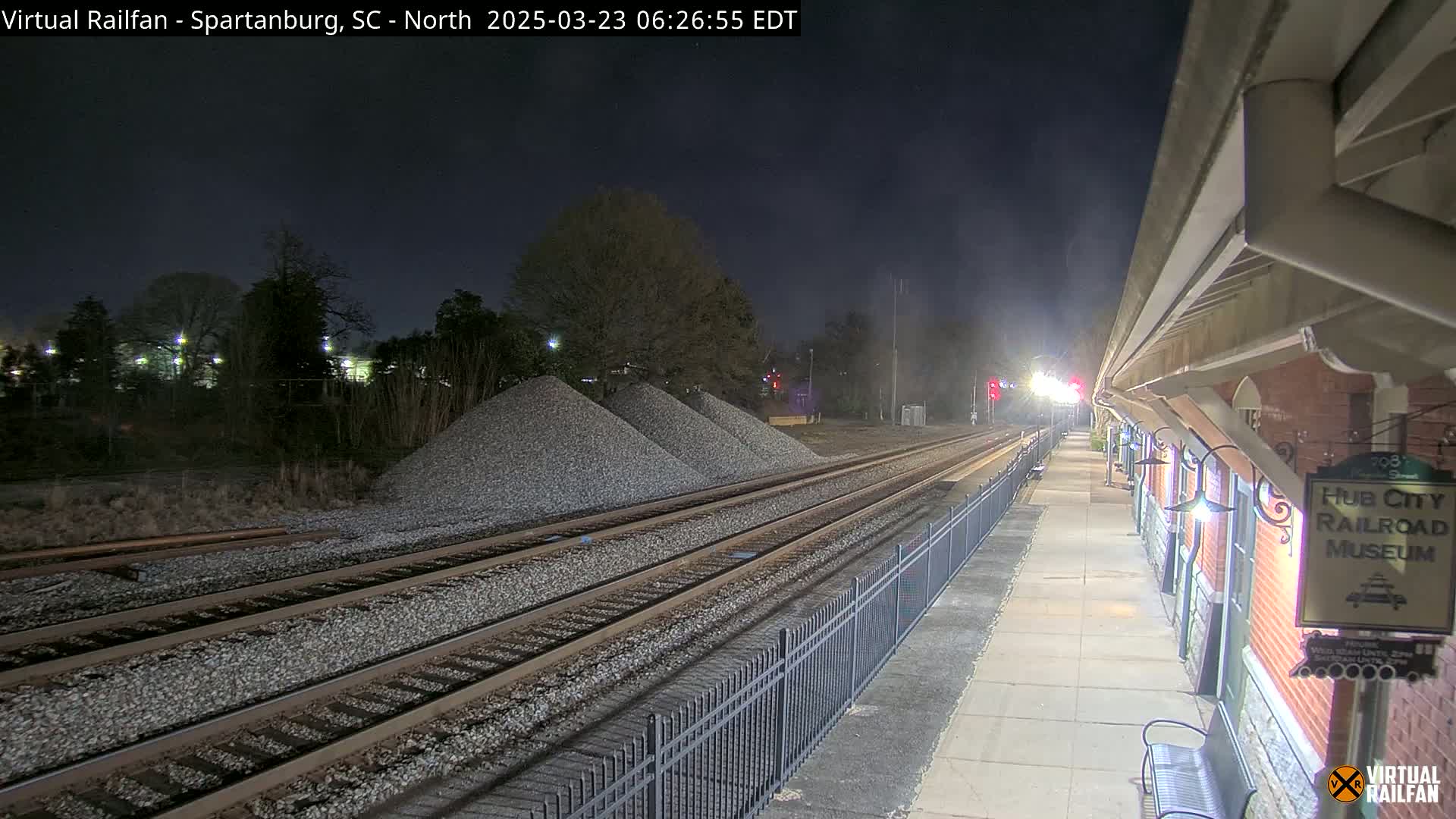At night, railroad tracks extend from a train platform next to a brick building, with piles of gravel nearby.
