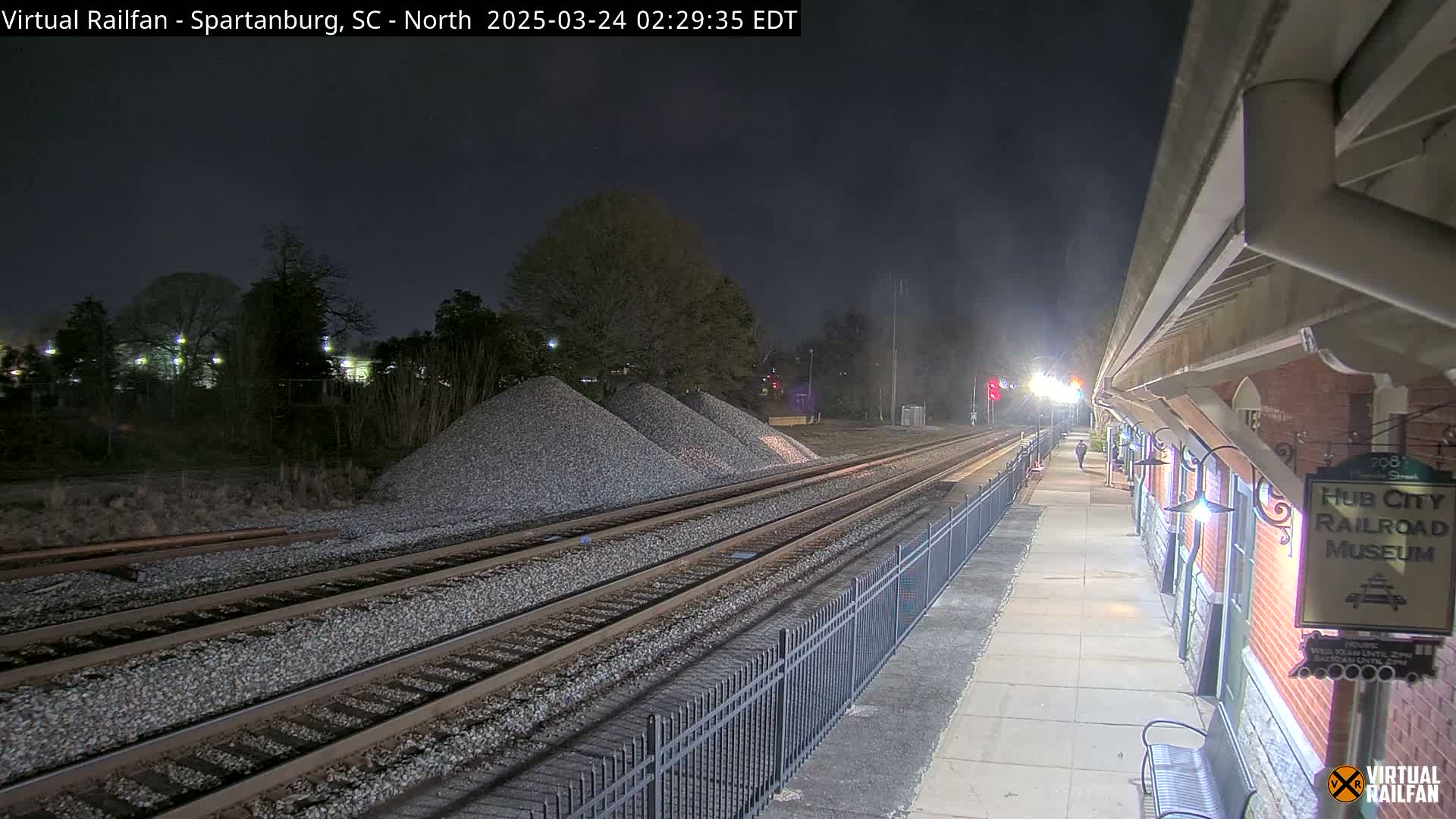 At night, train tracks extend from a station platform with piles of gravel nearby under a dark sky.