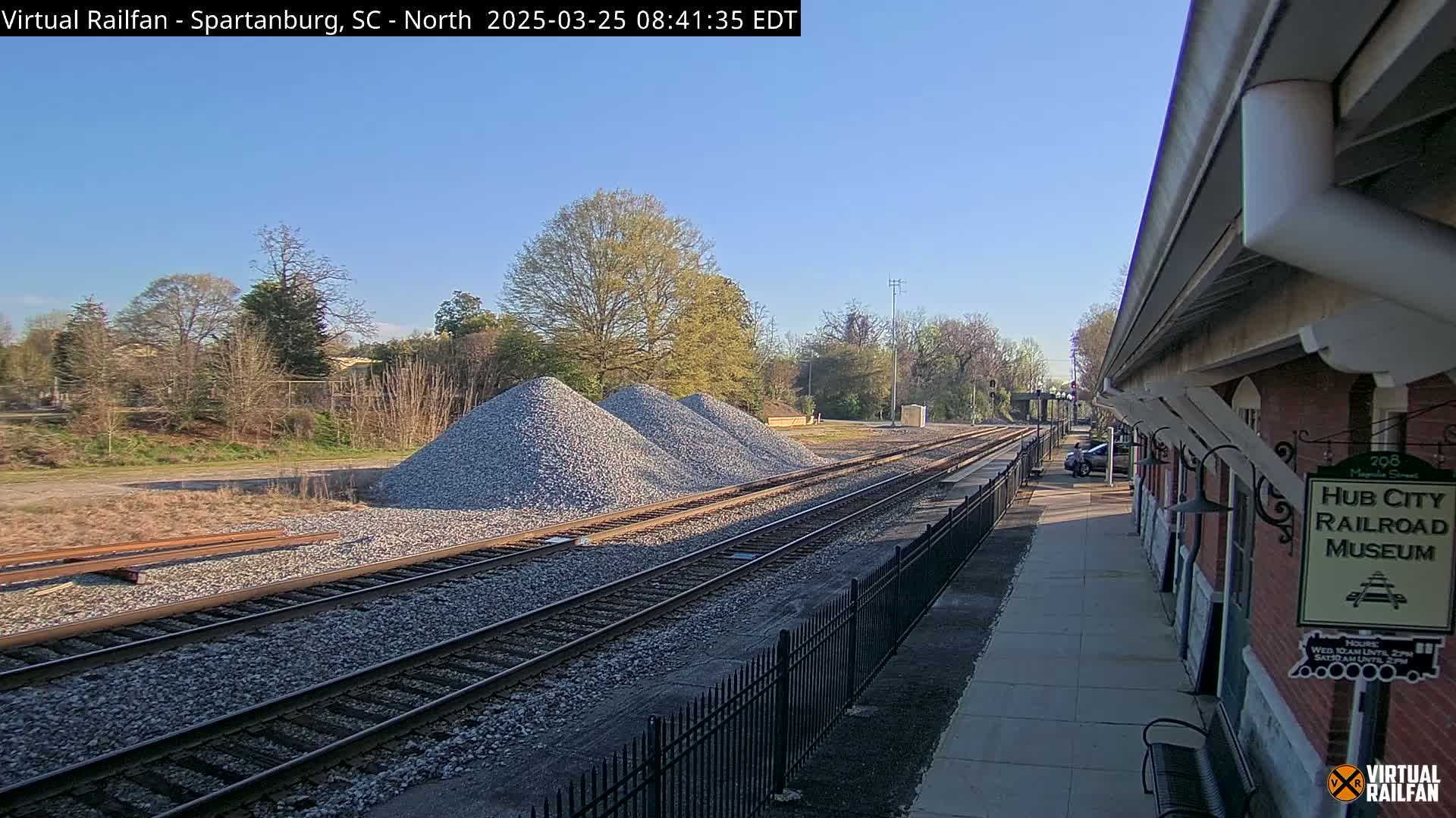 Several piles of gravel are beside railroad tracks next to a brick building on a sunny day.