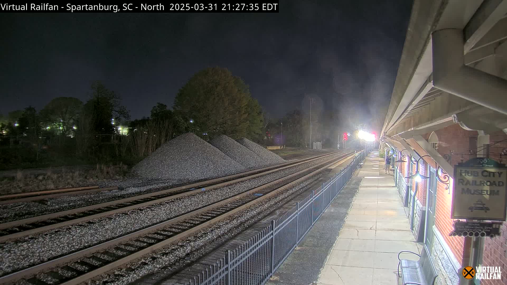 A nighttime view of train tracks leading to a railroad museum, with piles of gravel nearby under a dark, clear sky.