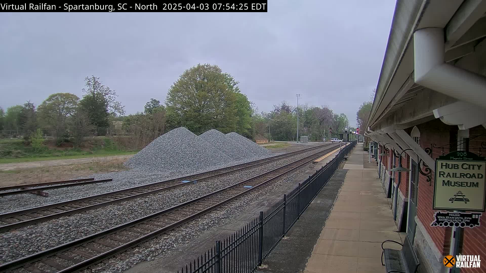 Three piles of gravel sit beside railroad tracks next to a brick railroad museum building on an overcast day.