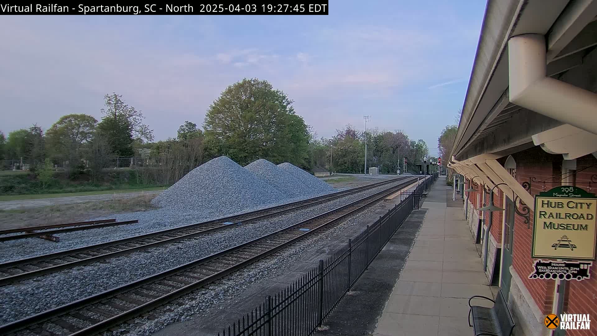 Three piles of gravel sit beside railroad tracks next to a brick building under a twilight sky.