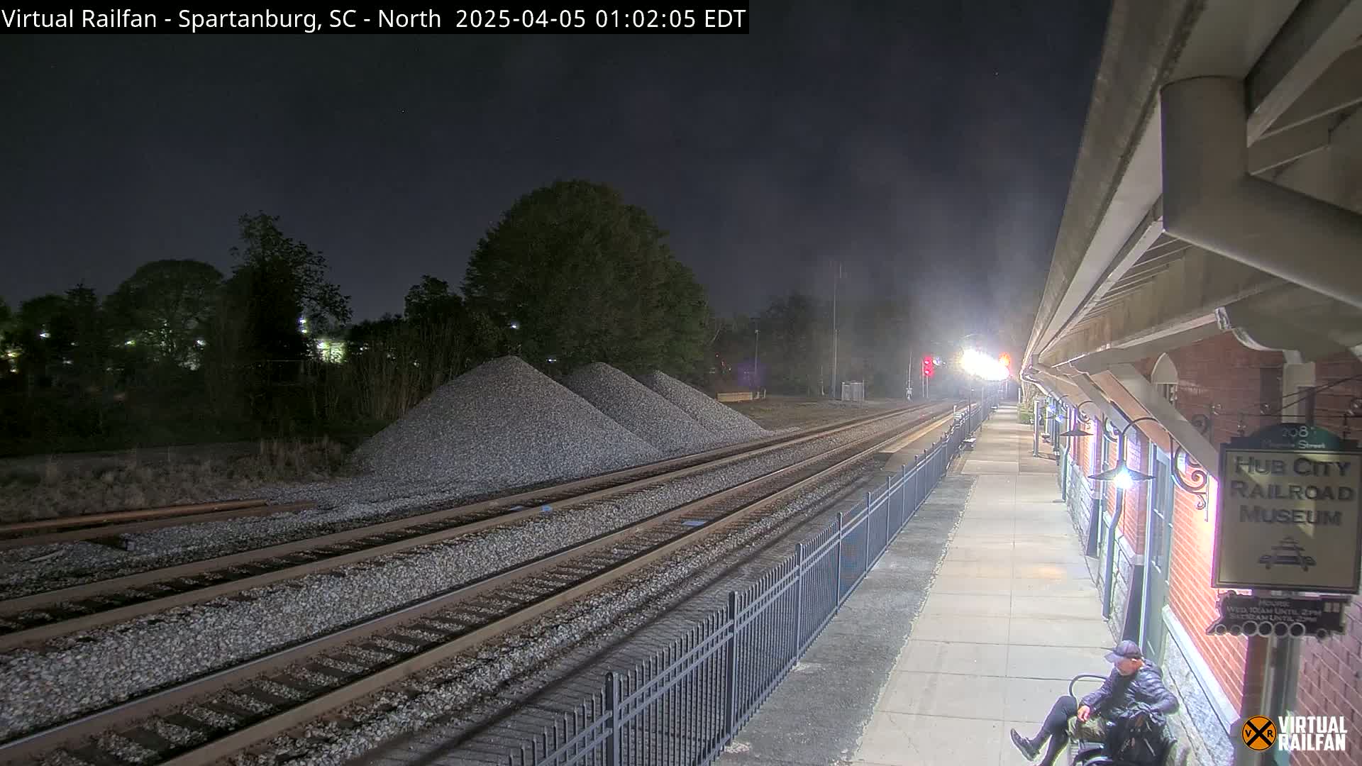 A nighttime view of train tracks and a railroad museum platform, with piles of gravel nearby under a dark, clear sky.