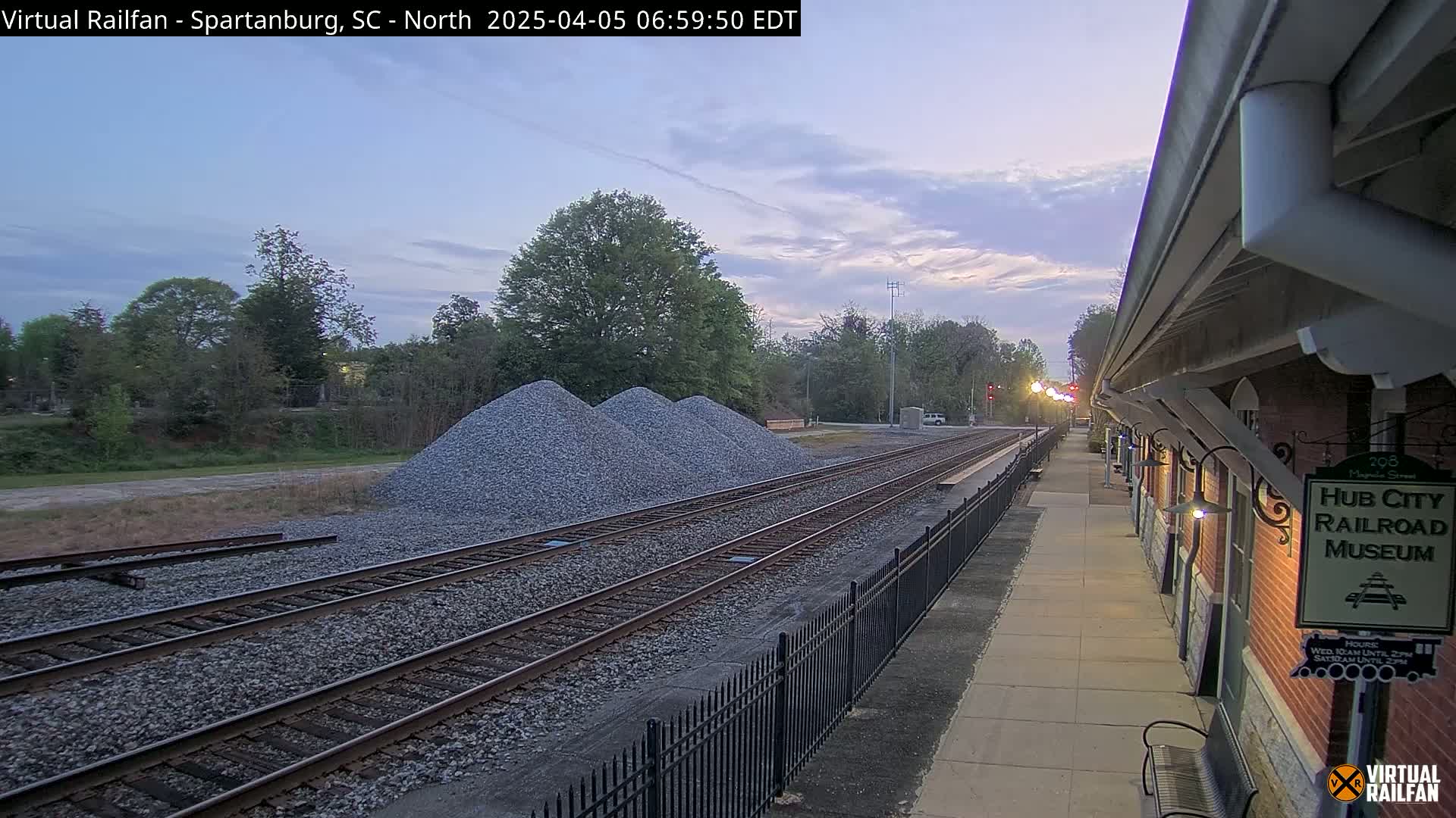 A twilight view of railroad tracks beside a brick building, with piles of gravel nearby.