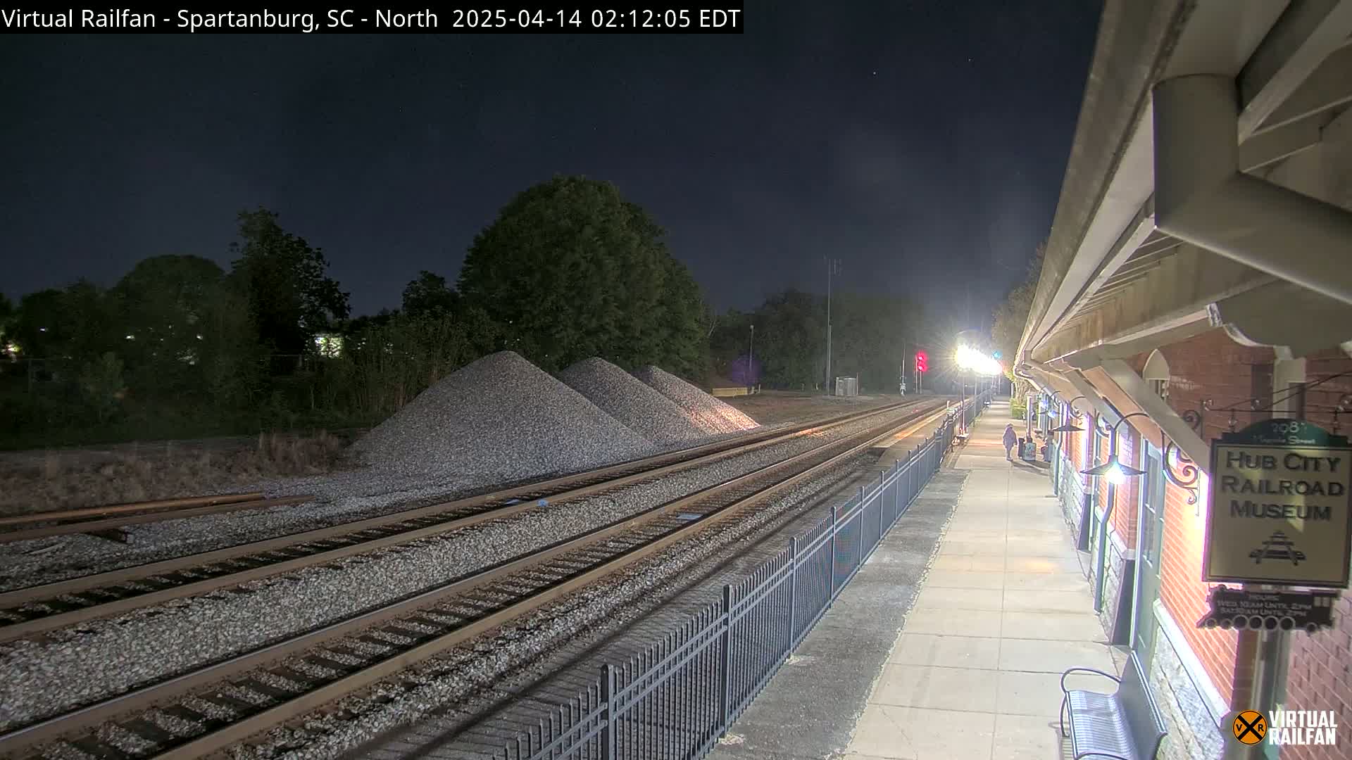 A nighttime view of train tracks next to a railroad museum, with piles of gravel visible nearby under a clear, dark sky.