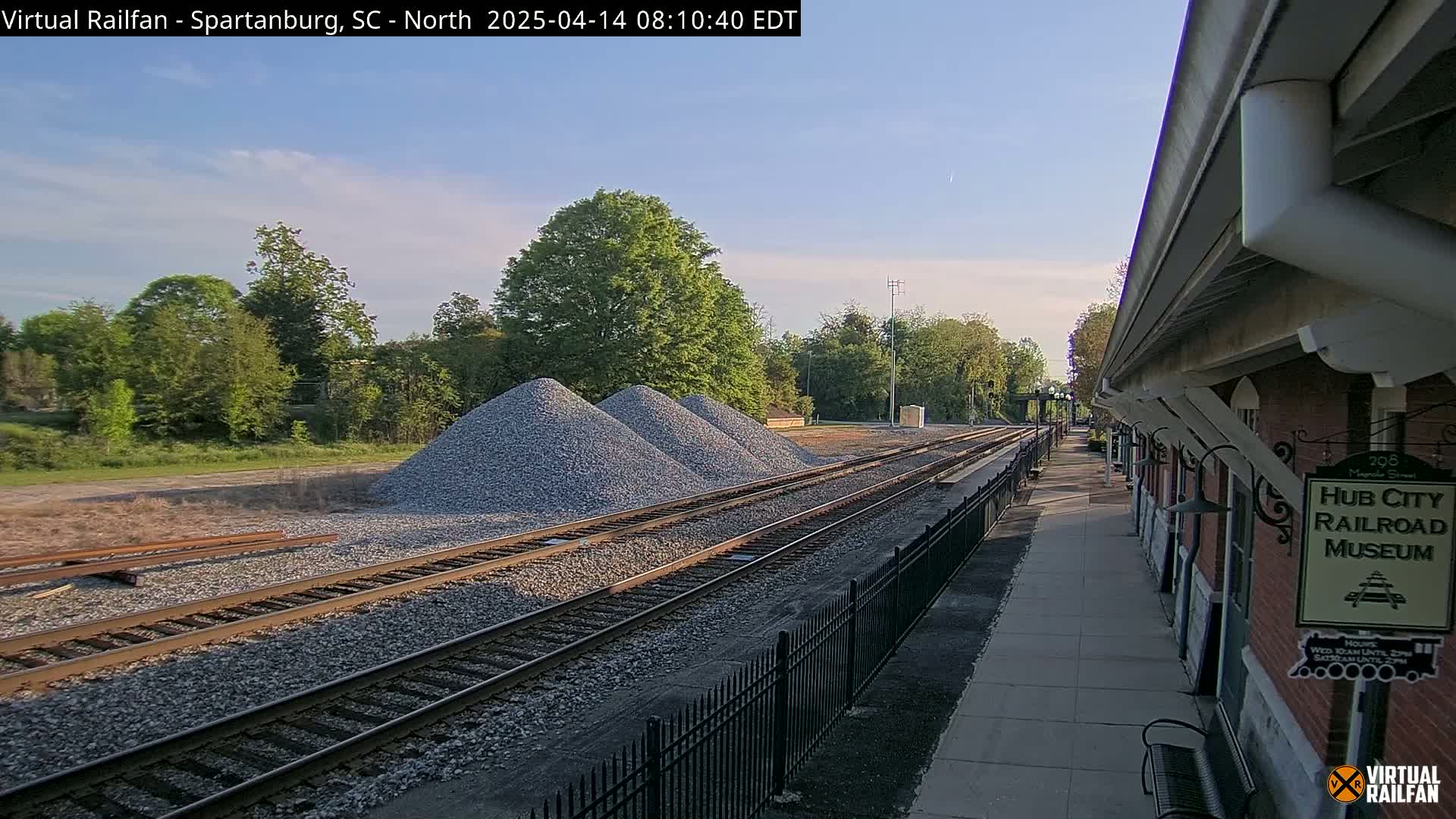 Three piles of gravel sit beside railroad tracks next to a railroad museum on a partly sunny day.