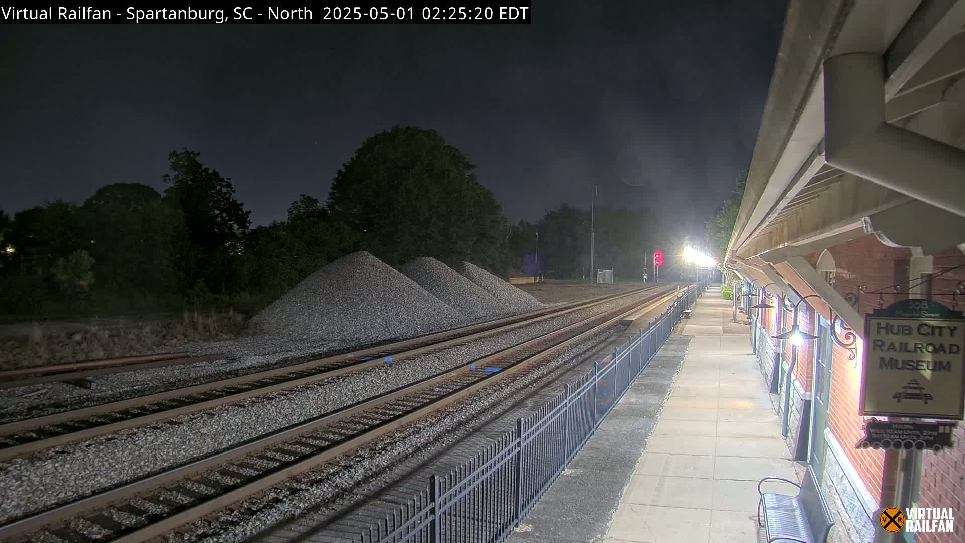 A nighttime view of railroad tracks next to a brick building, with piles of gravel nearby under a dark sky.