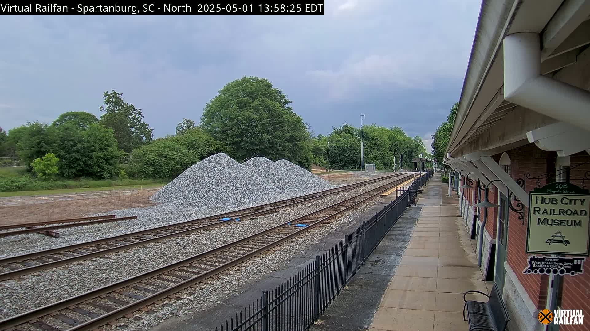 Three piles of gravel sit beside railroad tracks next to a brick railroad museum building on an overcast day.