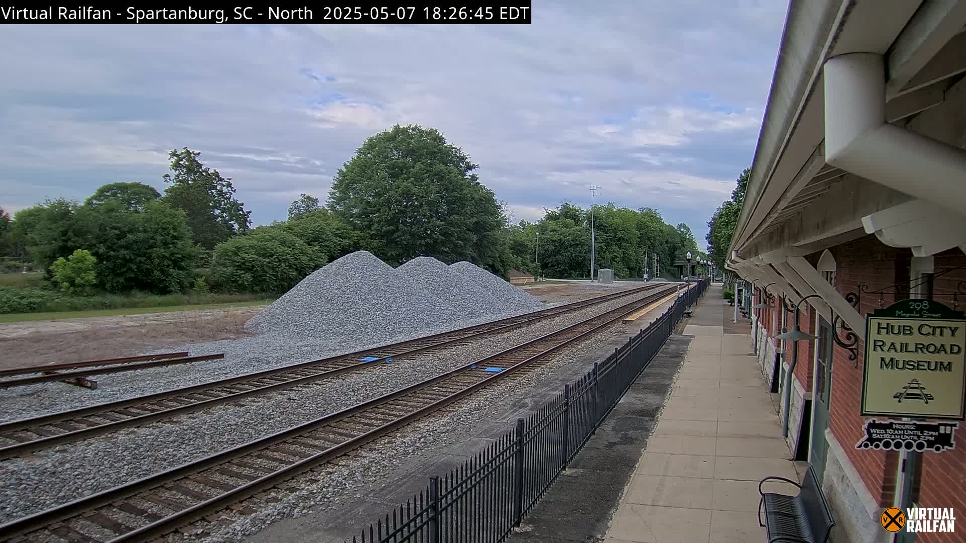 Several piles of gravel sit beside railroad tracks next to a brick building on a partly cloudy day.