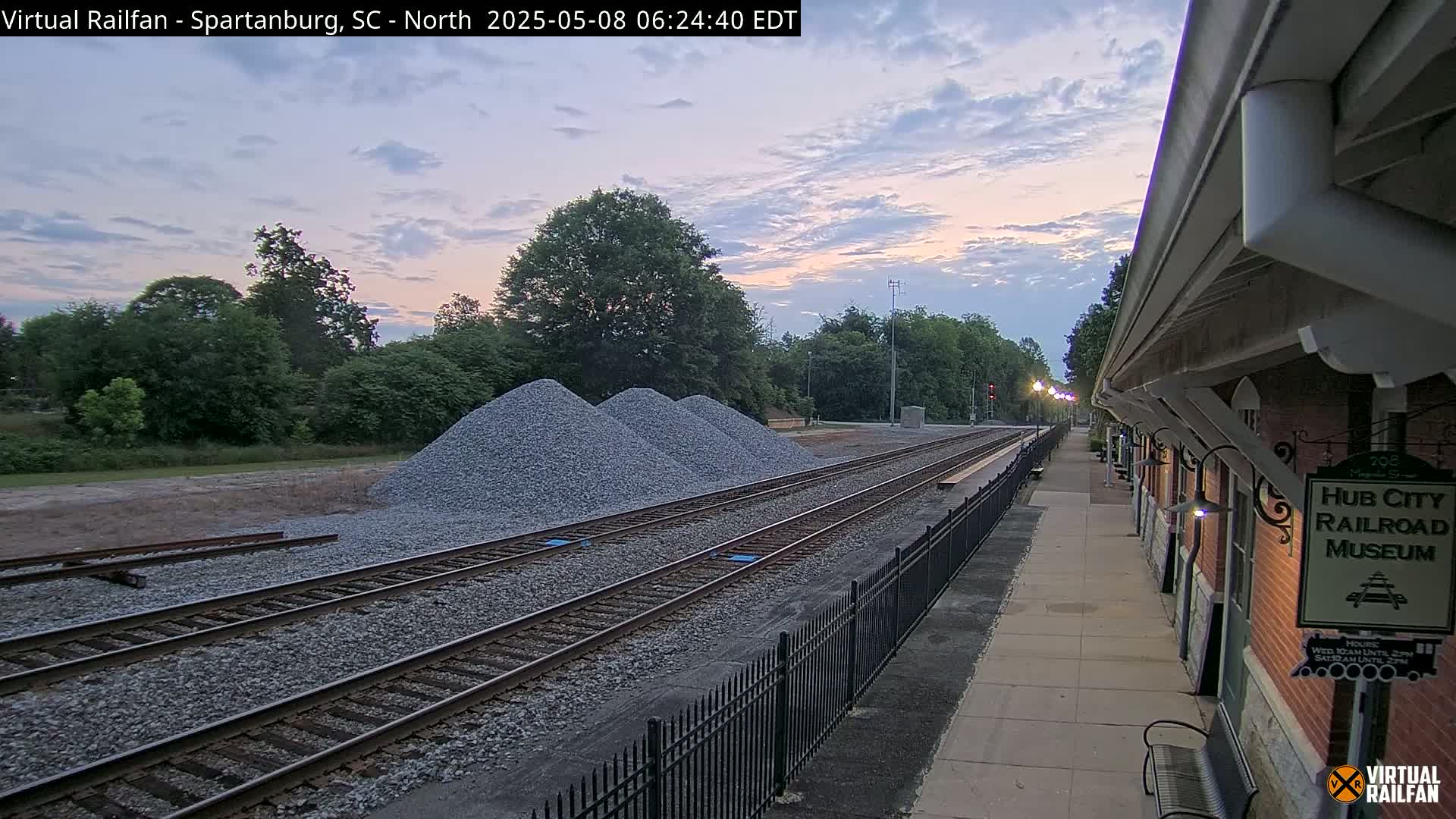 Three piles of gravel sit beside railroad tracks next to a brick building at twilight.