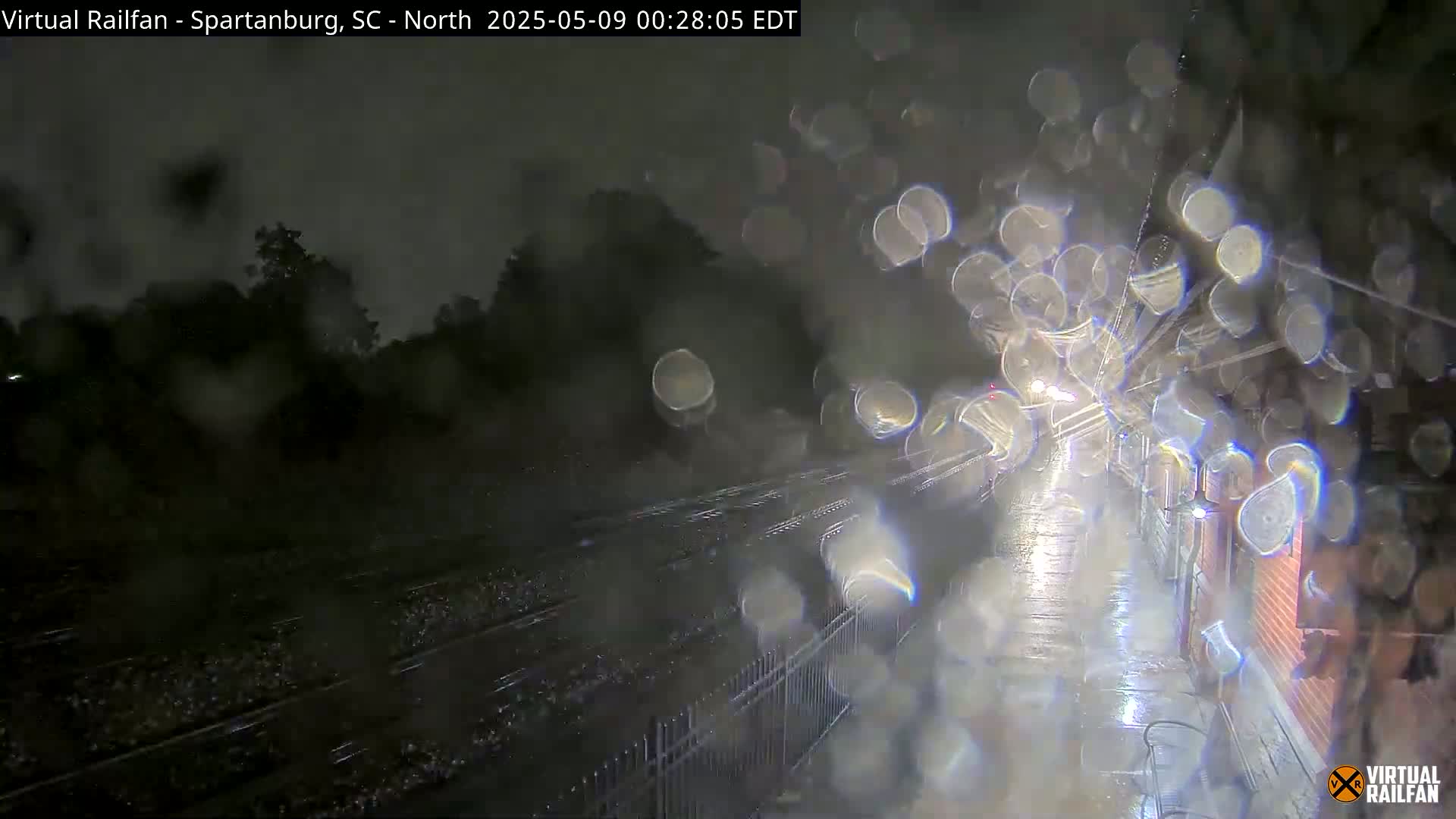 A nighttime view of rain-slicked railroad tracks and a nearby street, seen through a rain-covered window.