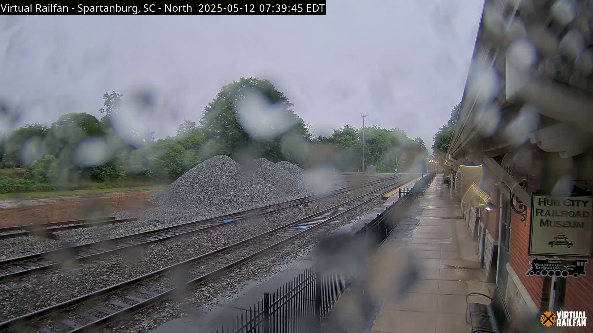 Rain falls on a railway scene with piles of gravel near train tracks next to a railroad museum.