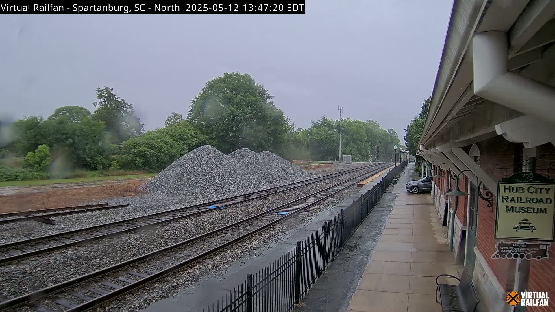 A rainy view of train tracks with piles of gravel beside them, next to a railroad museum on a platform.