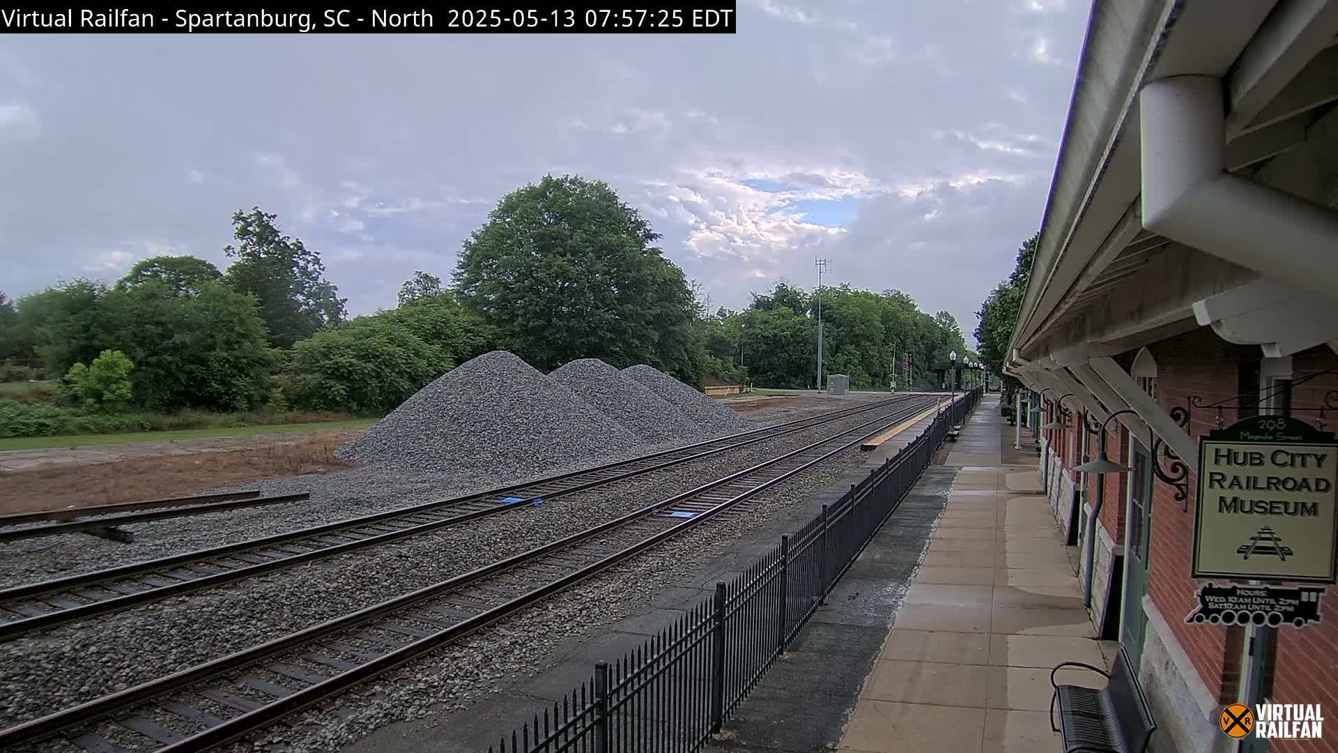 Several piles of gravel are situated beside train tracks next to a brick building, under an overcast sky.