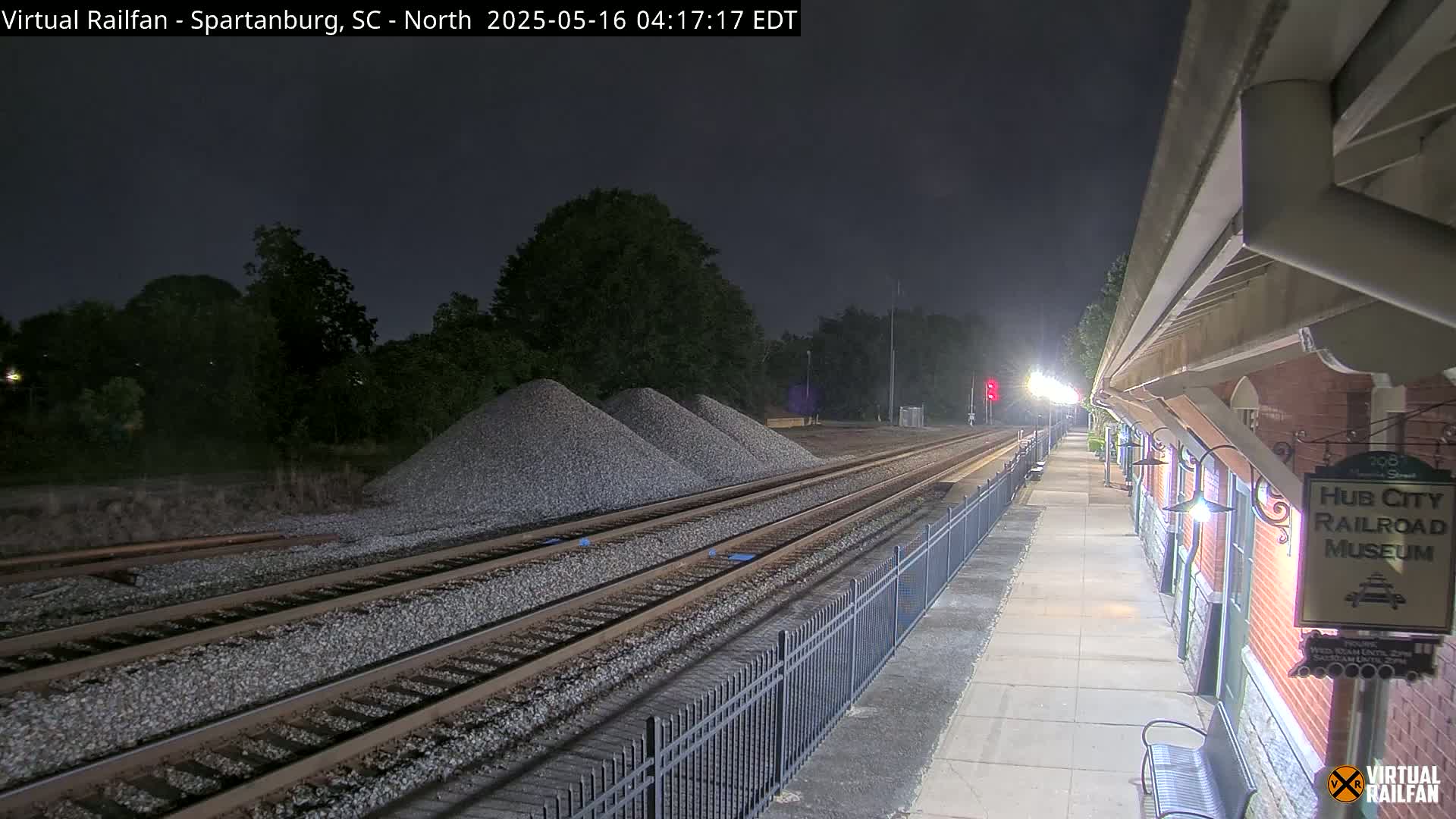 At night, train tracks extend from a railroad museum platform past several piles of gravel under a clear, dark sky.
