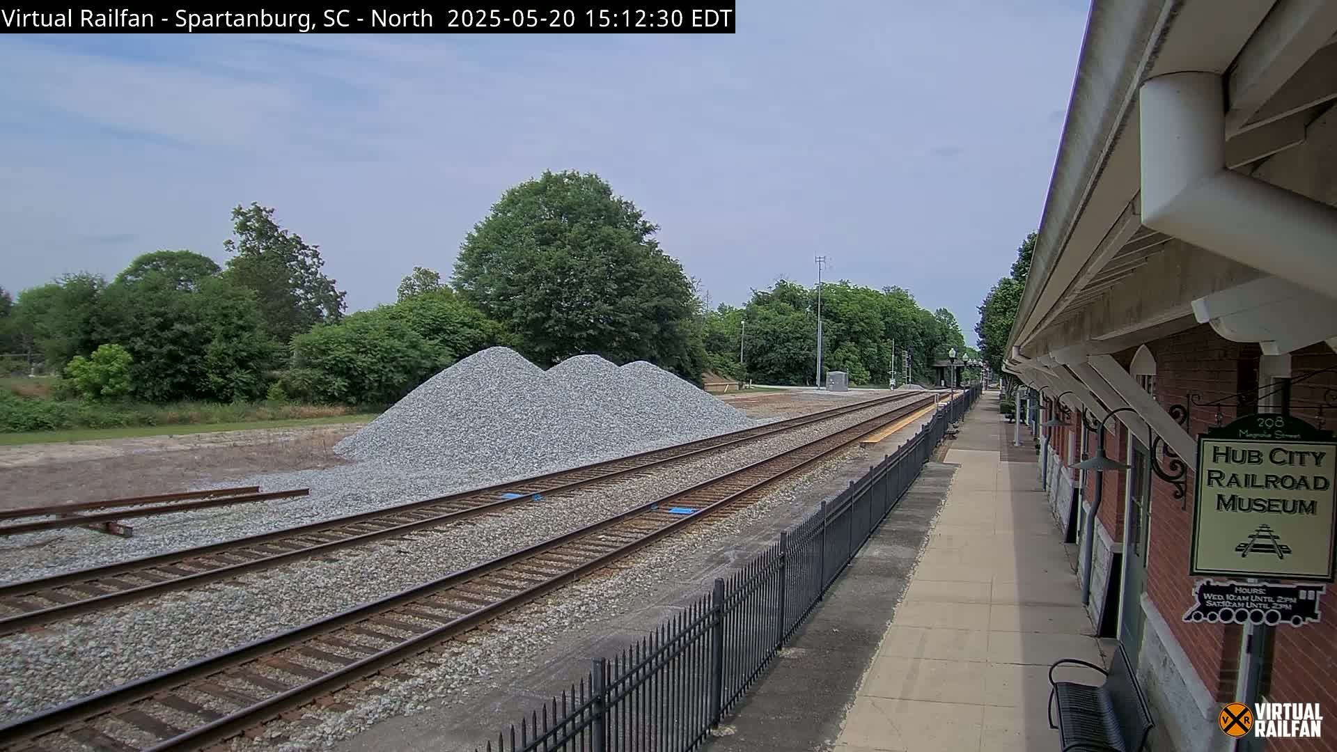 Three piles of gravel sit beside railroad tracks next to a brick building, under a mostly cloudy sky.