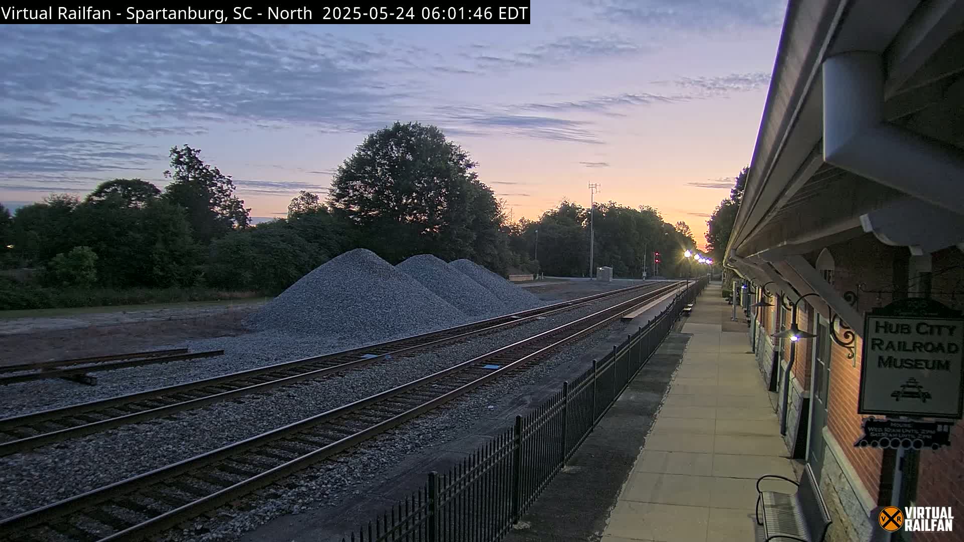 Train tracks with piles of gravel next to a railroad museum at sunrise.