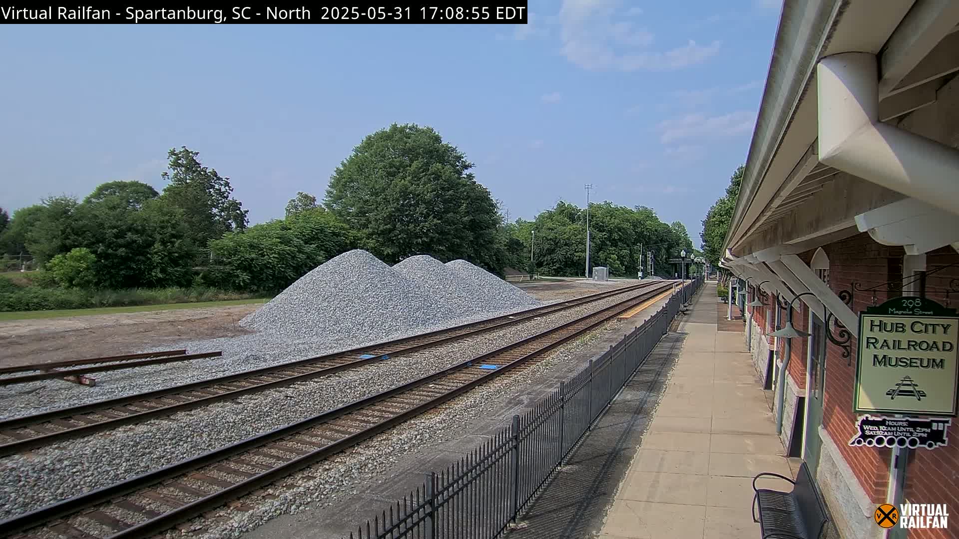A sunny day reveals railroad tracks next to a brick railroad museum building with piles of gravel nearby.