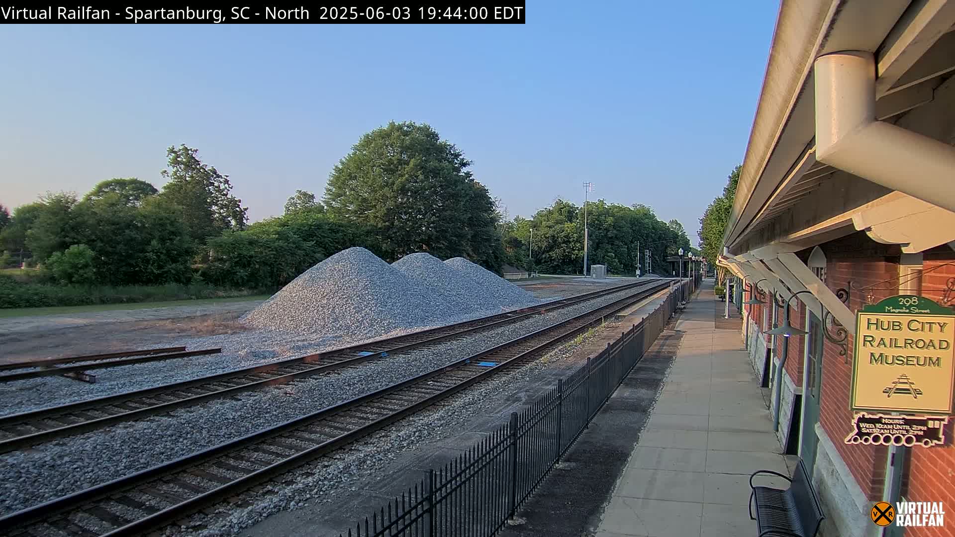 Under a clear sky, a railway track with three piles of gravel lies adjacent to a brick railroad museum building.