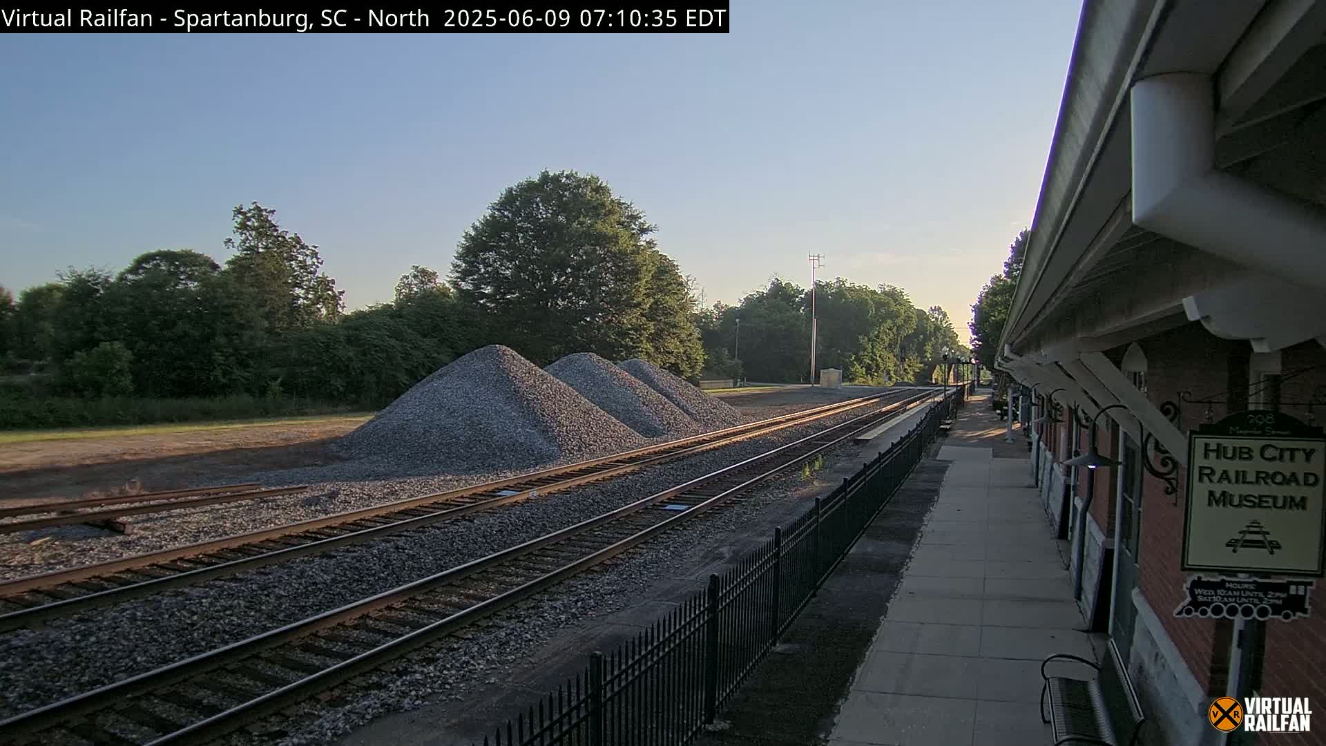 Under a clear sky, three piles of gravel sit beside a train track next to a railroad museum.