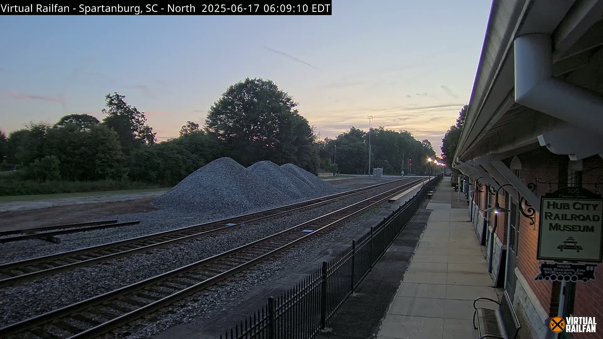 Under a twilight sky, railroad tracks extend toward a brick building next to piles of gravel.