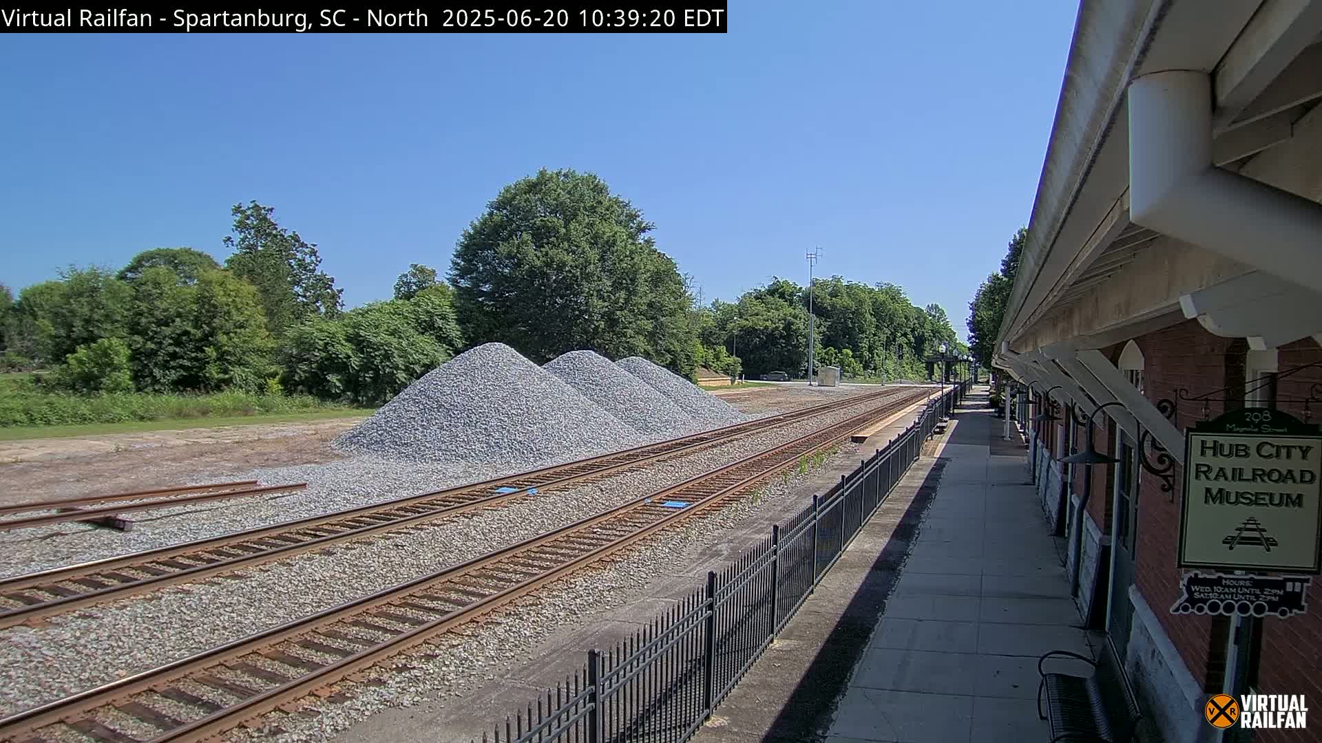 Three piles of gravel sit beside train tracks next to a brick railroad museum under a clear blue sky.