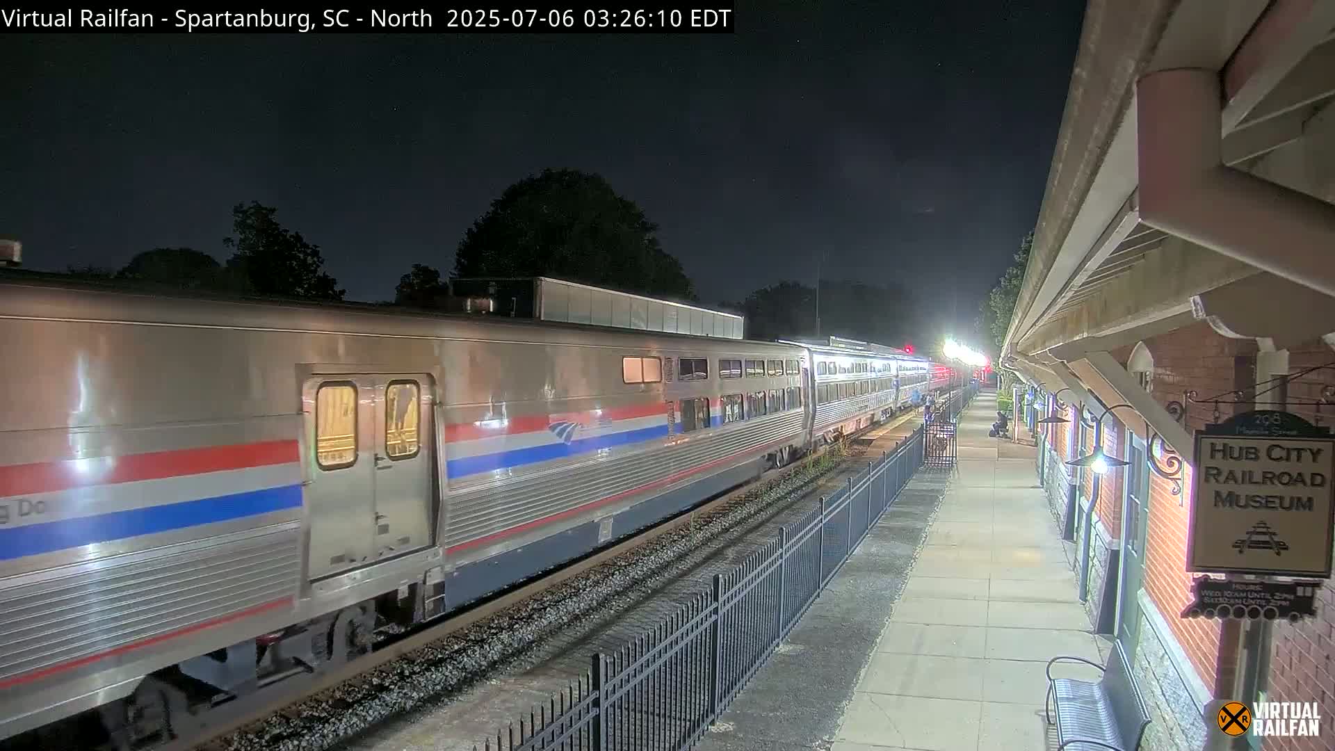 A passenger train is passing through a nighttime train station.