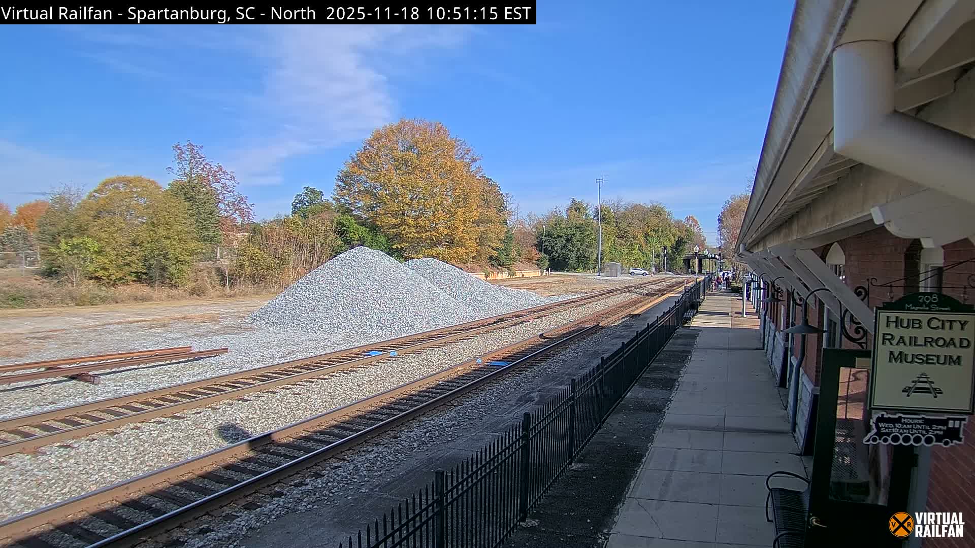 At night, a long freight train carrying orange shipping containers passes by a railroad museum platform.