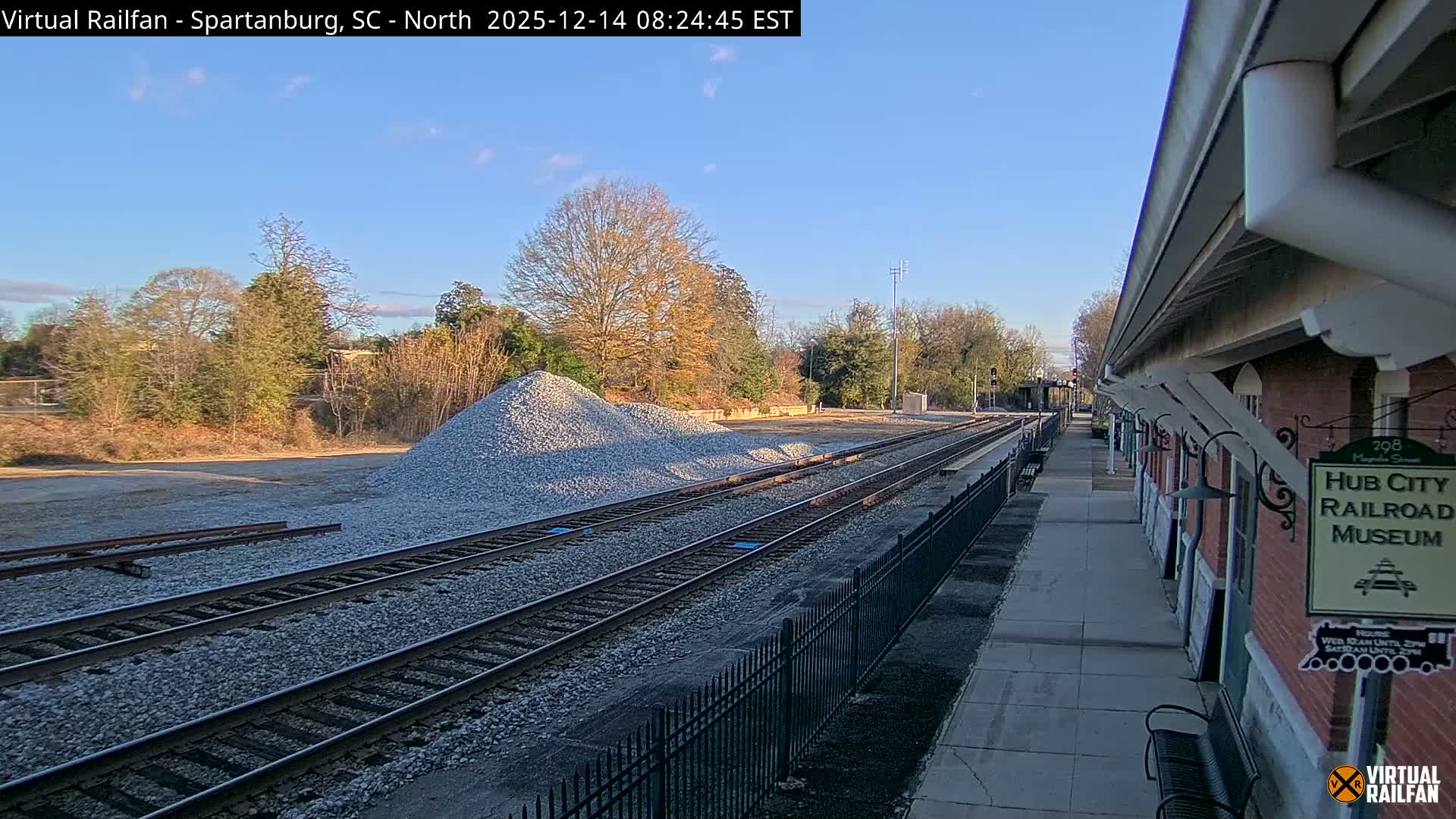 A rainy nighttime scene reveals multiple train tracks stretching into the distance alongside a dimly lit platform with benches, all viewed through a heavily rain-streaked lens.