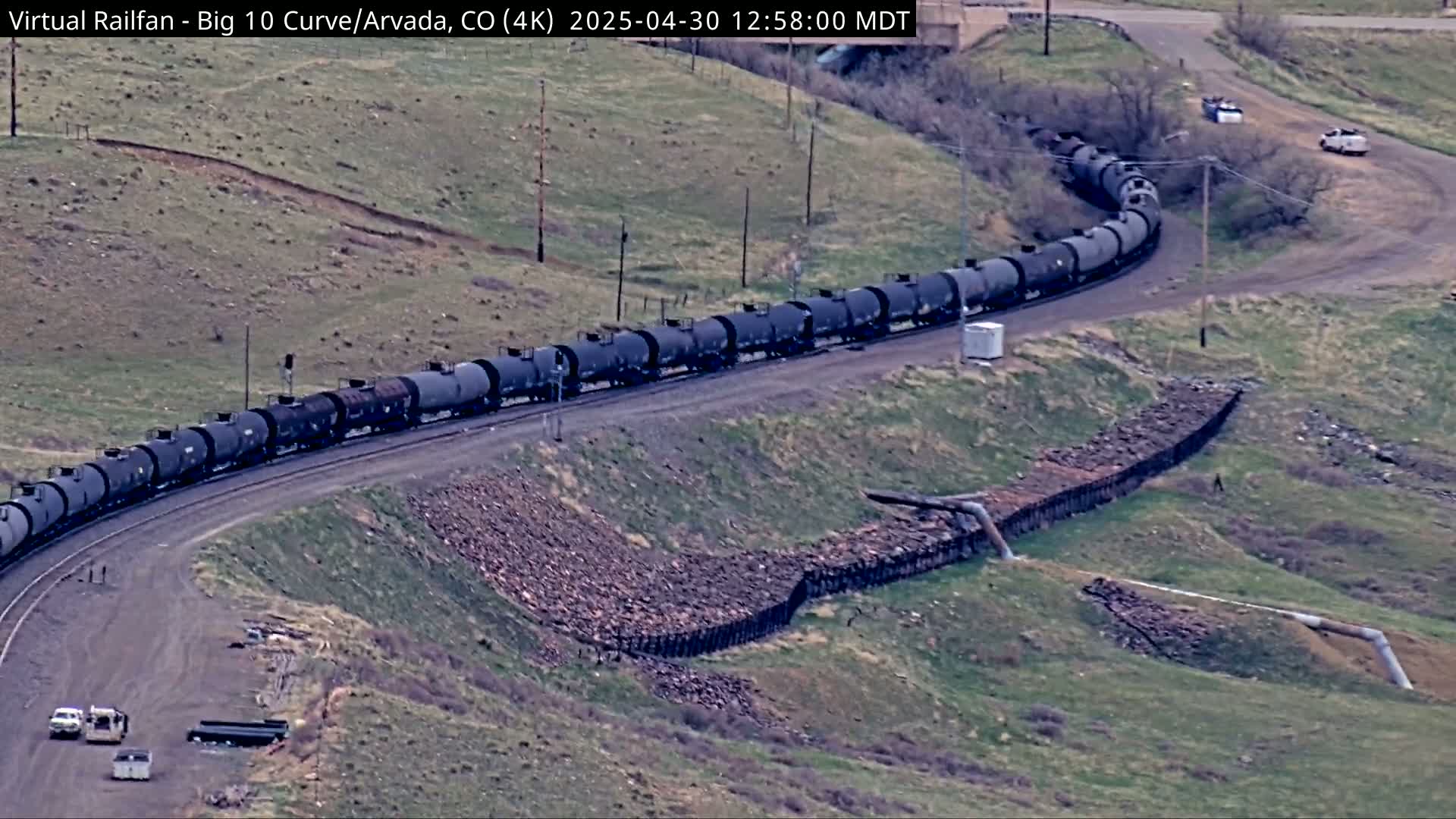 A long freight train of tanker cars curves around a hillside on a sunny day.