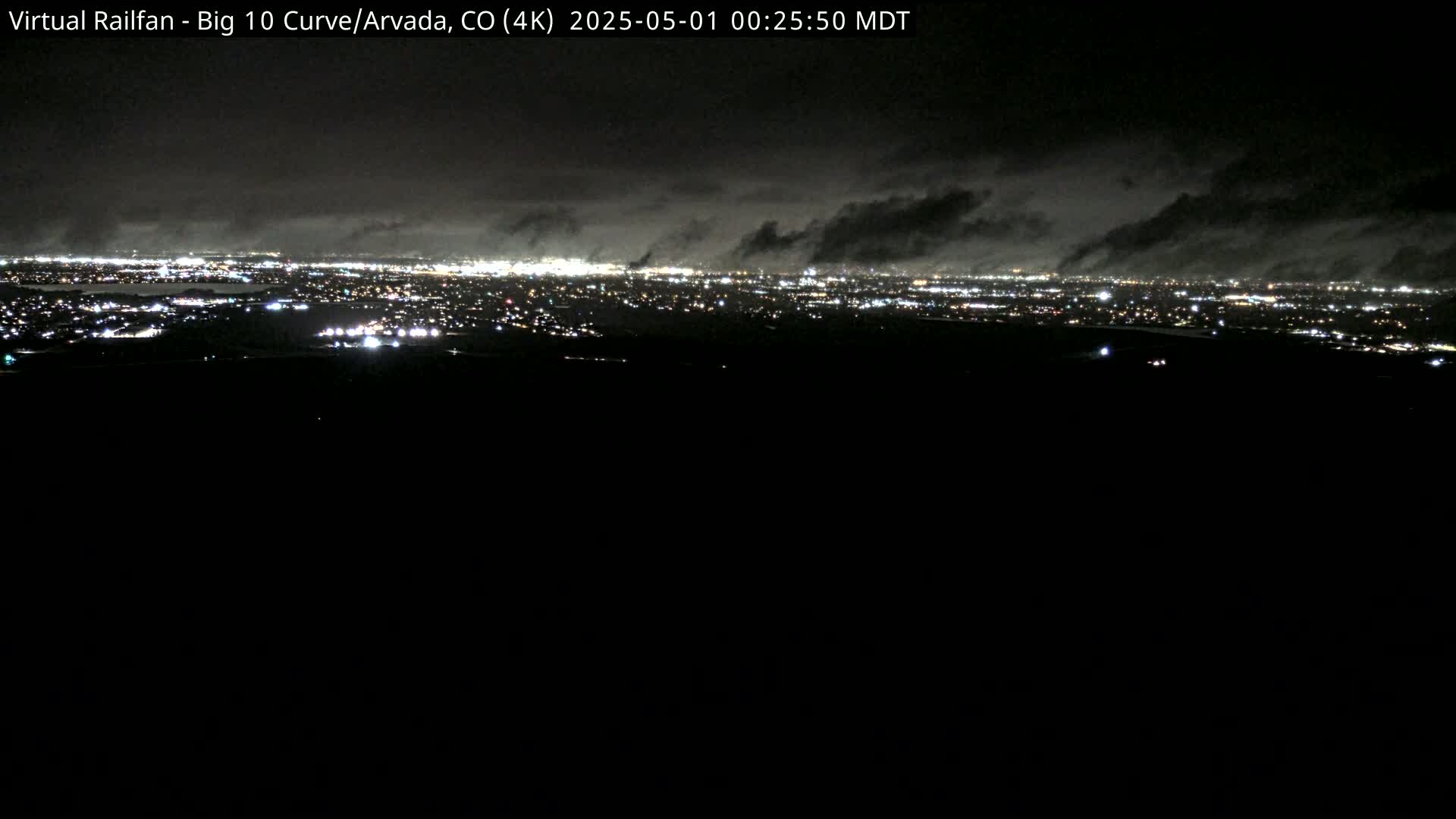 A nighttime, high-angle view of a city illuminated by lights under a cloudy sky.
