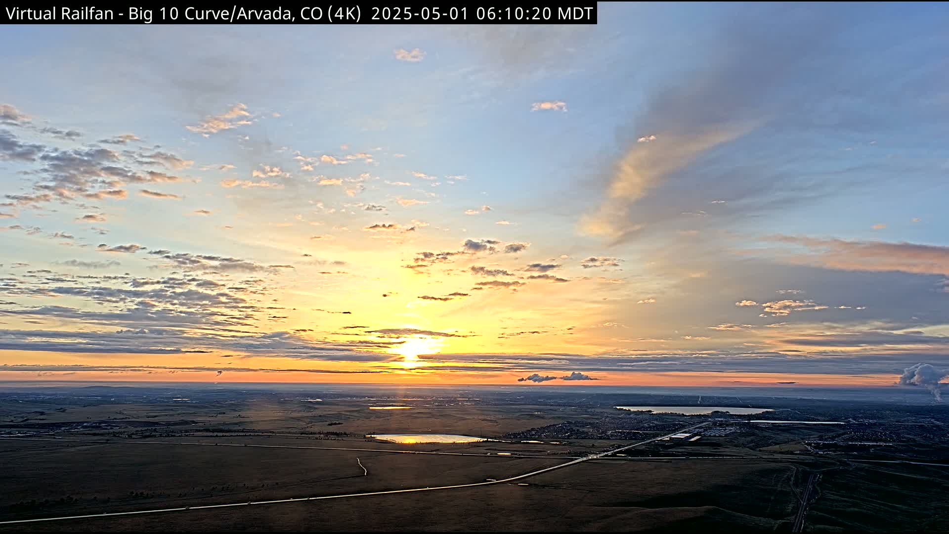 A sunrise over a flat landscape with scattered clouds and some low-lying smoke or haze in the distance.